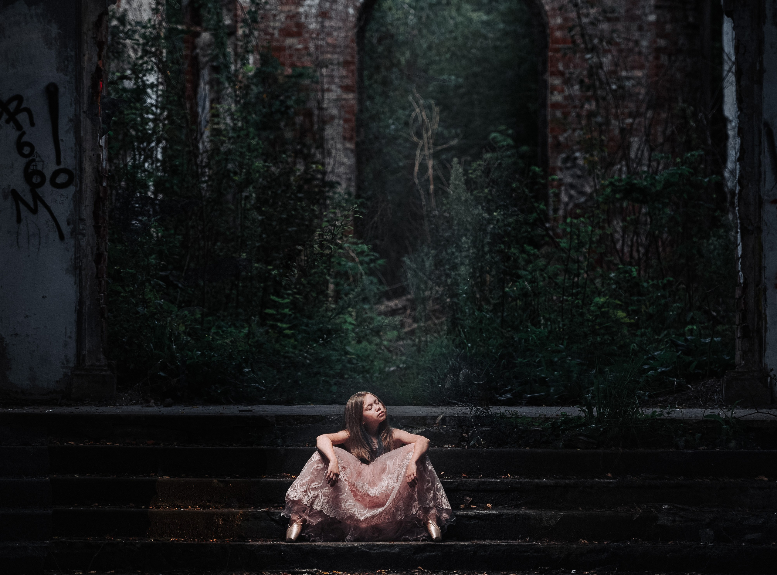 Девочка в красивом платье и пуантах сидит на лестнице  на фоне кирпичной стены