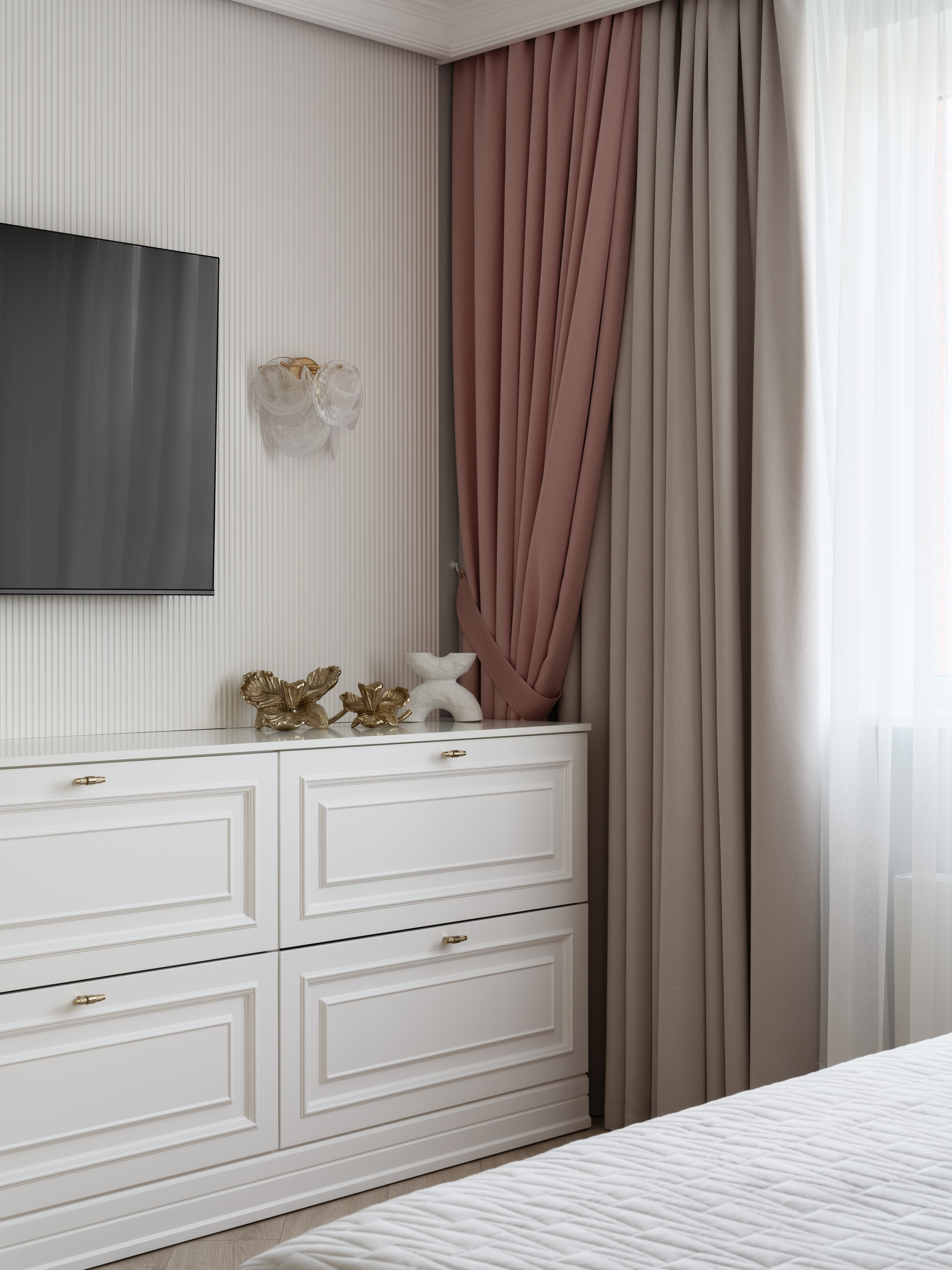 Белый классический комод с золотыми ручками, настенным ТВ и декоративными элементами. Шторы в розово-бежевых оттенках создают уютную атмосферу. Интерьер Евгении Ермошиной, фотограф Сергей Денисенко.