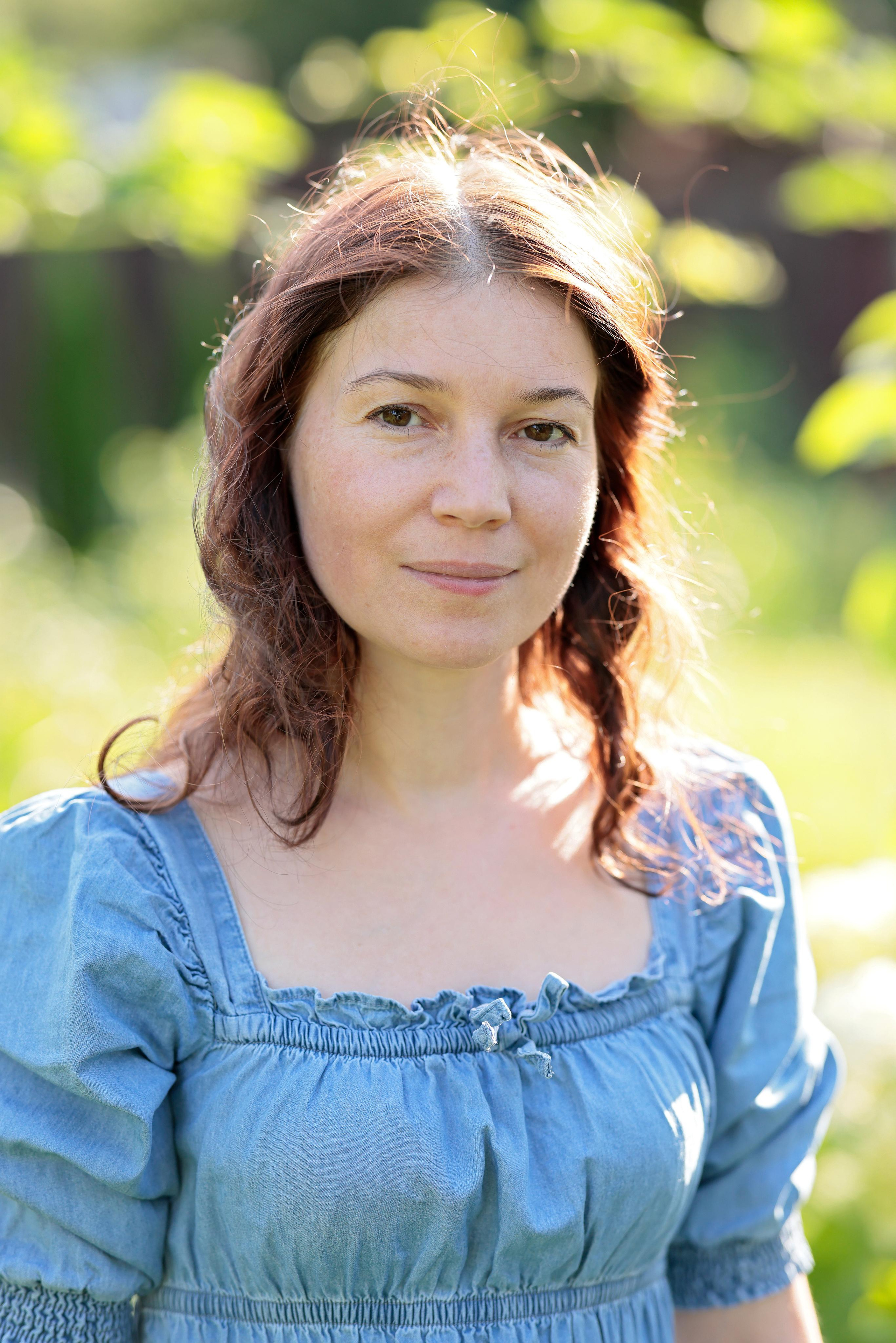 Портрет женщины в голубом платье на фоне зелени.