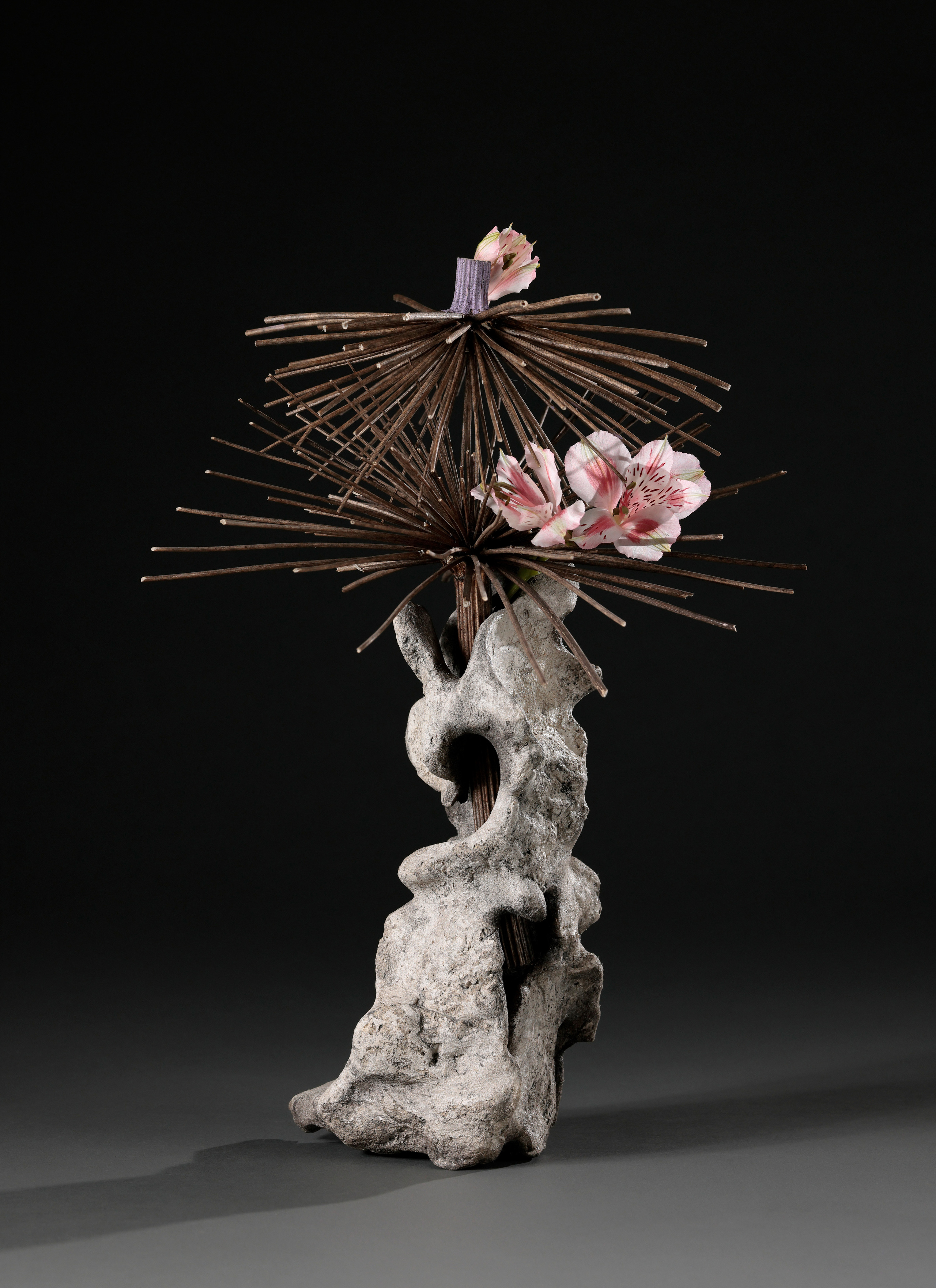 Икебана в бетонной вазе сложной формы ручной работы на тёмно-сером фоне.