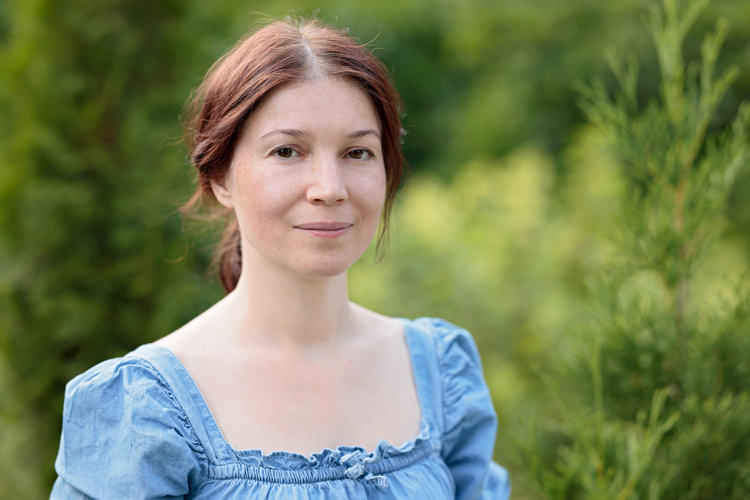 Портрет женщины в голубом платье на фоне зелени.