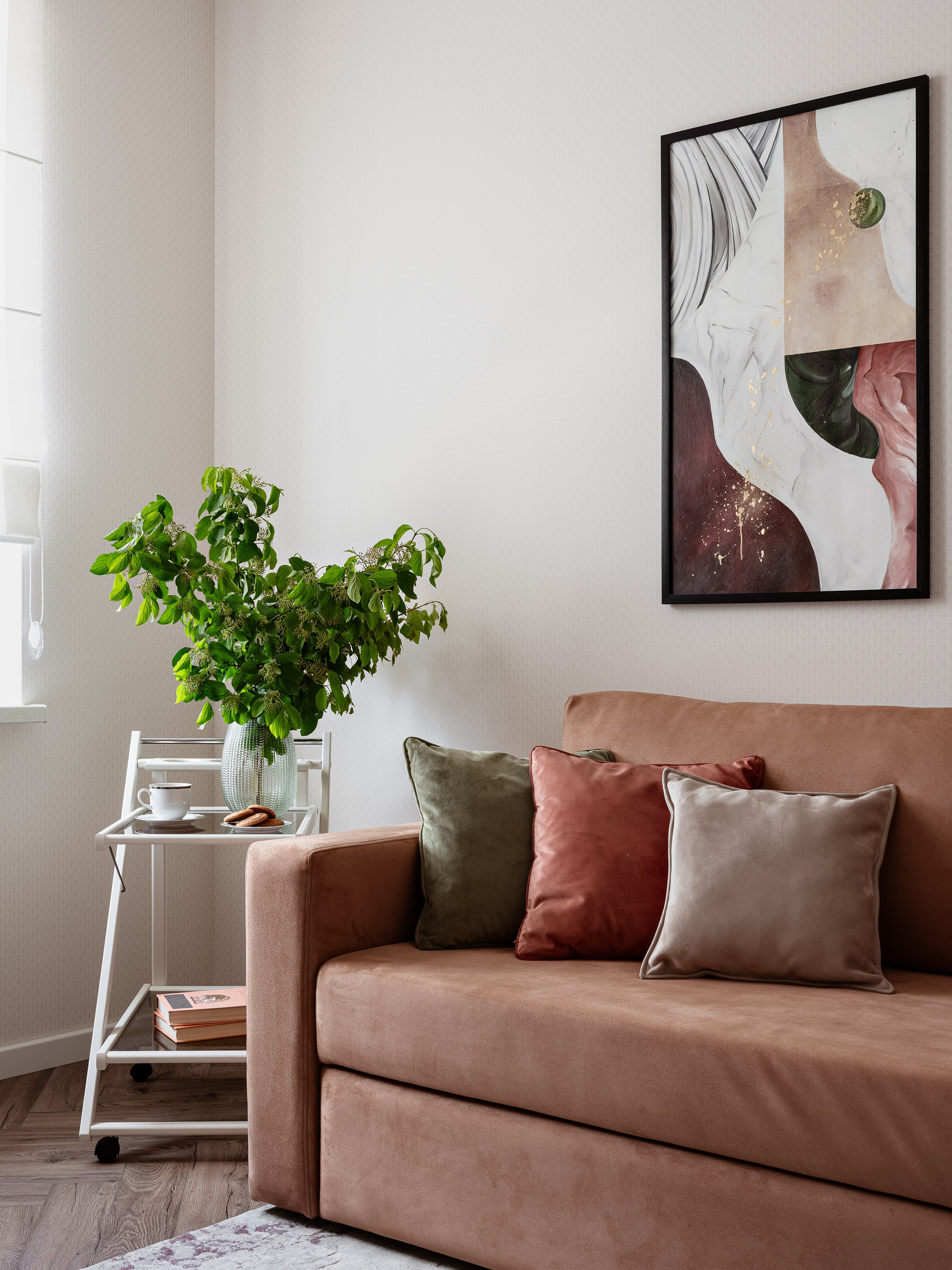 Светлая гостиная с мягким коричневым диваном и подушками, зелёное растение в стеклянной вазе на белом столике, современный интерьер с акцентом на натуральные оттенки, дизайнер Алина Чередниченко, фотограф Сергей Денисенко