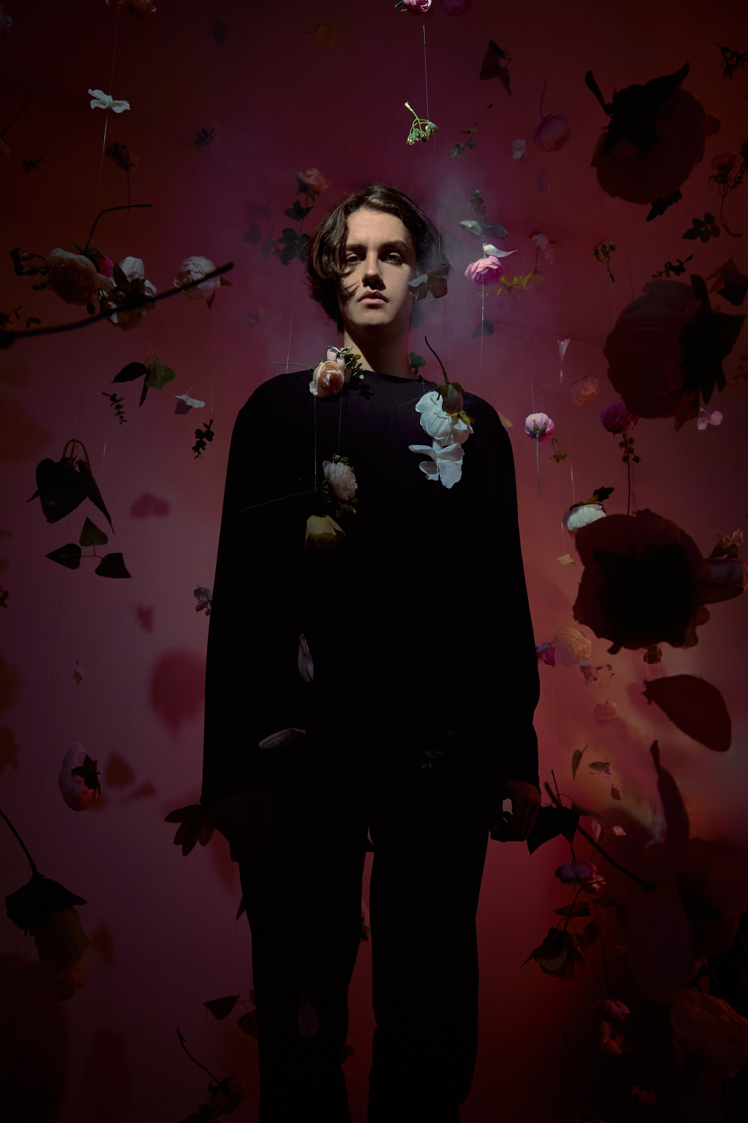 Портрет парня в черном среди цветов с красным светом