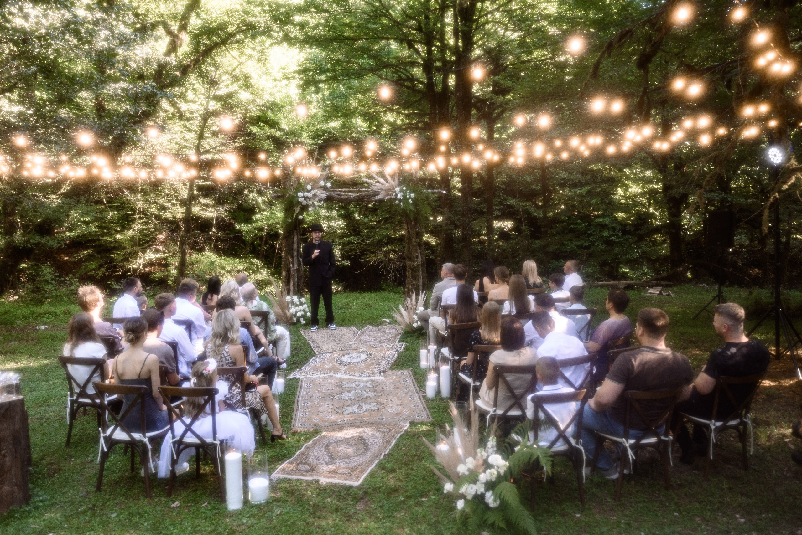 Церемония в лесу ведущий рассказывает историю молодых гостям сверху много гирлянд 