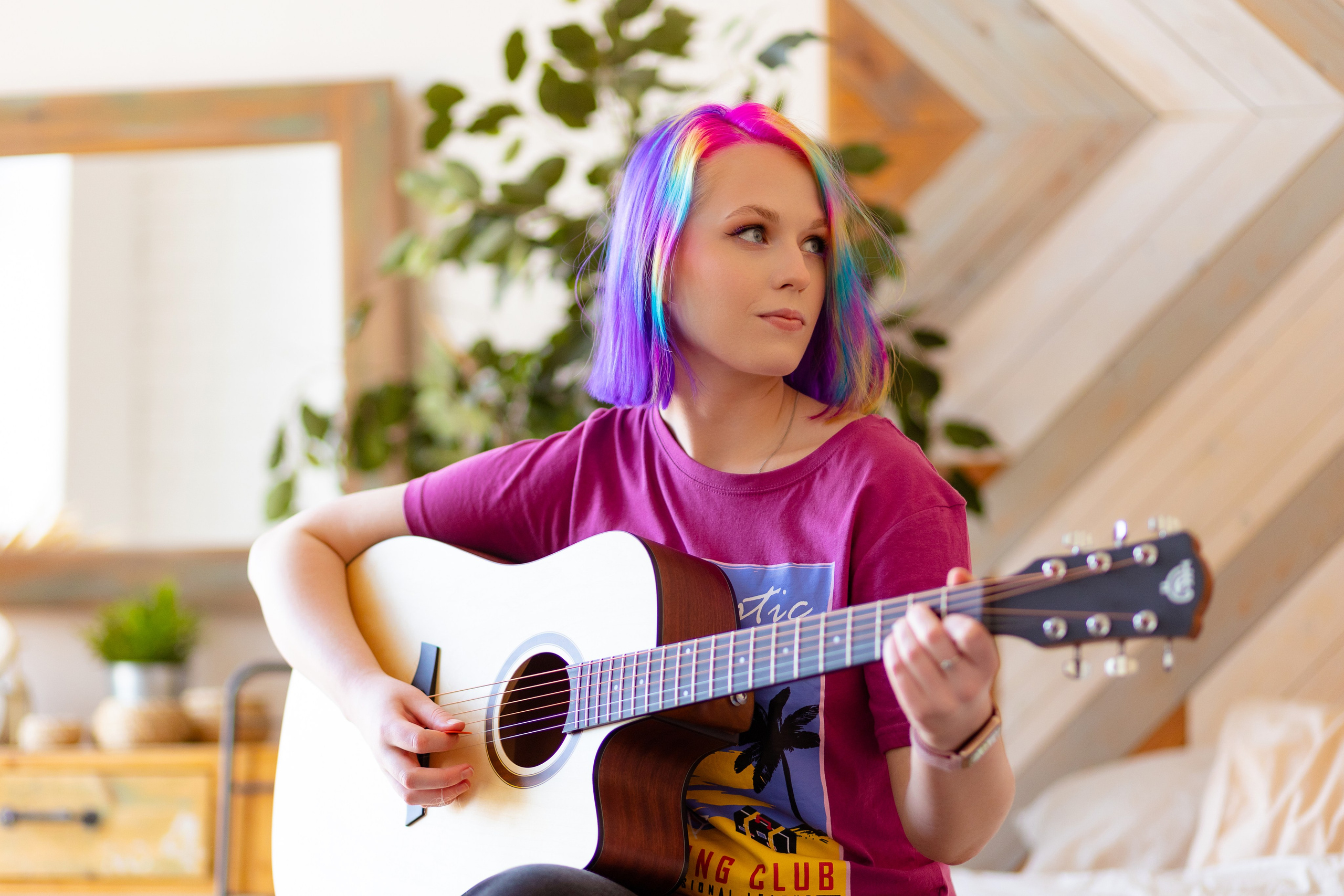 Девушка с цветными волосами играет на гитаре и смотрит в сторону.