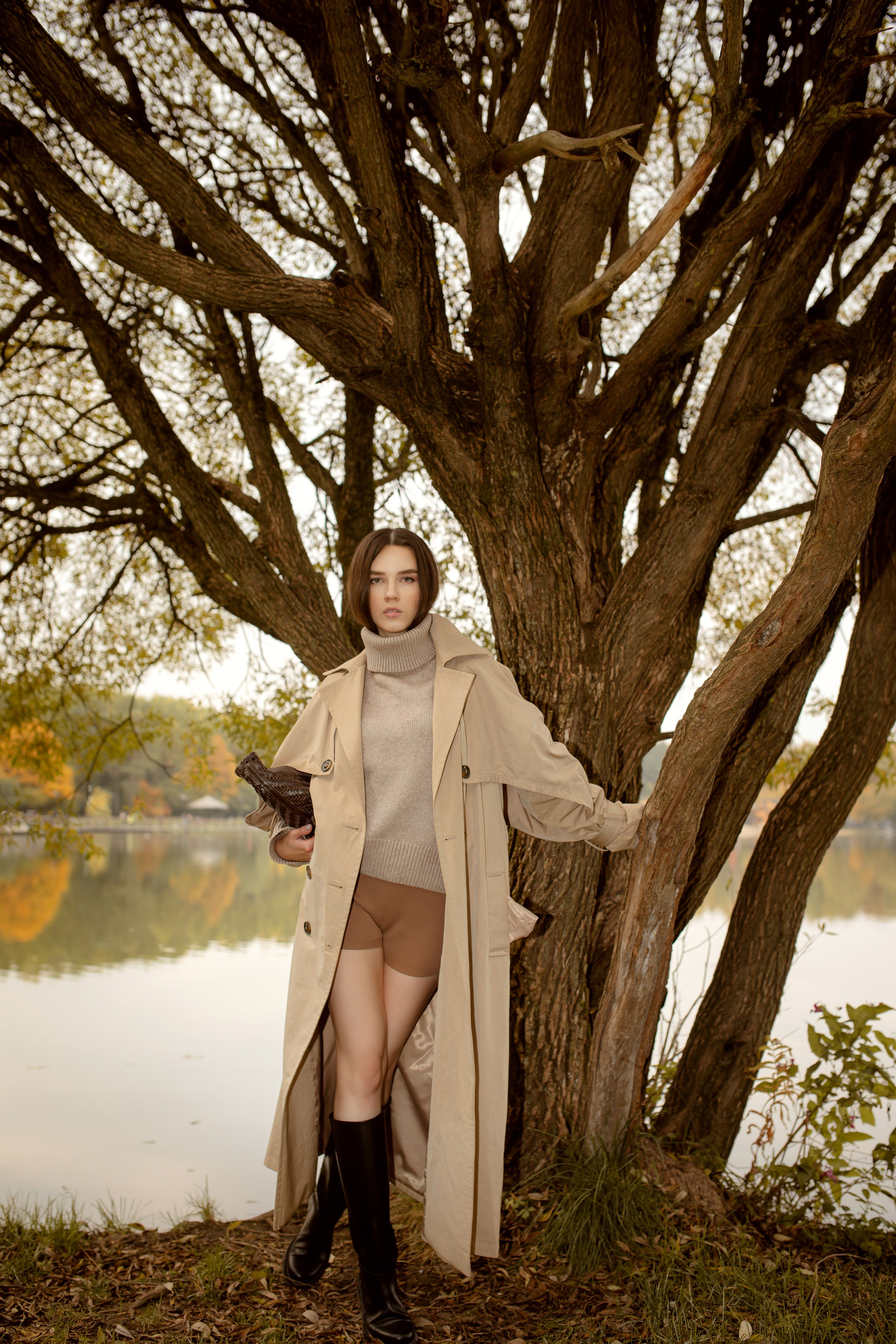 В модный современный одежды стоит рядом с деревом и держит его за ветви