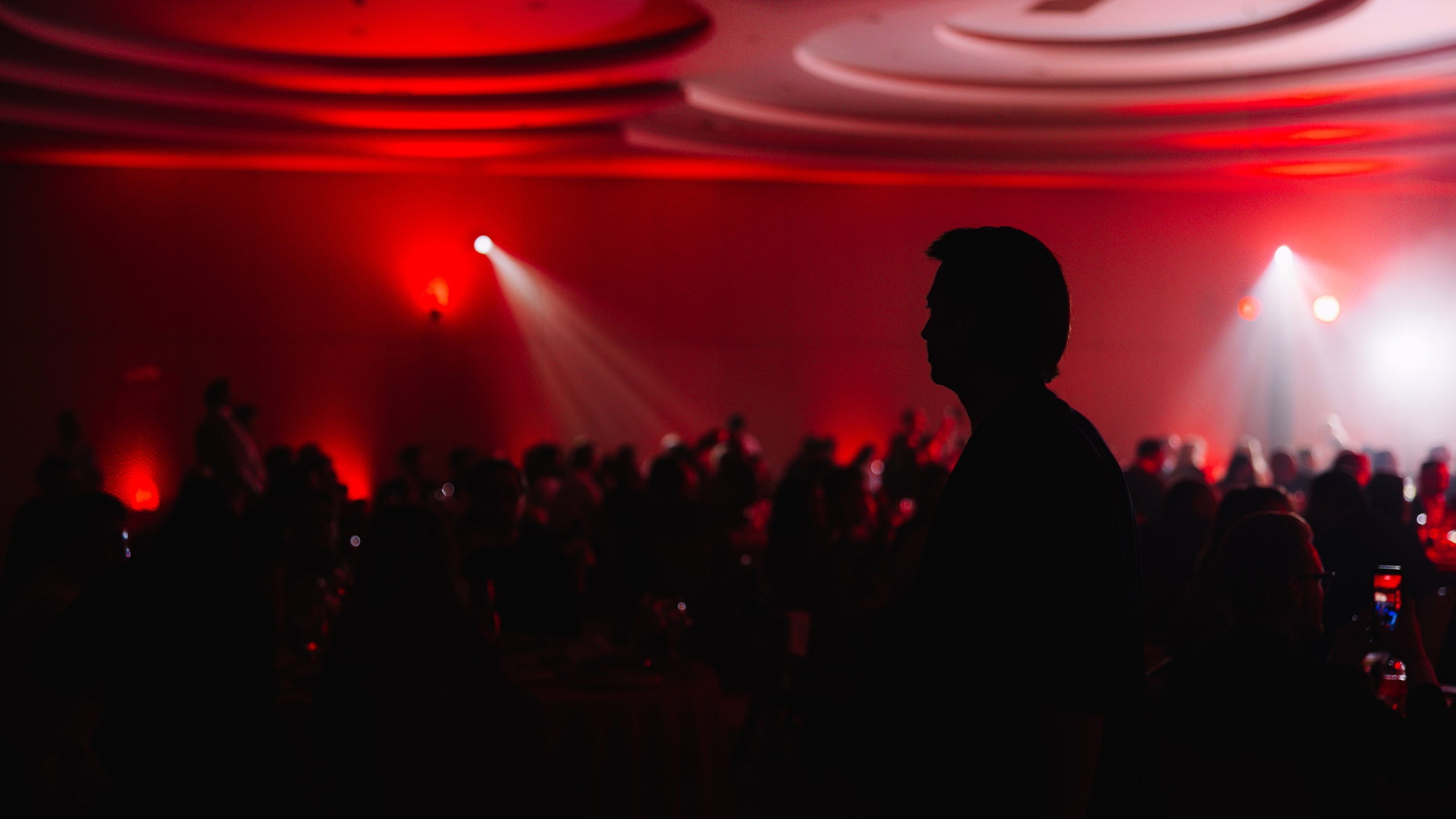 Атмосфера вечера: Силуэт участника в темном зале на фоне ярко подсвеченной красной сцены.