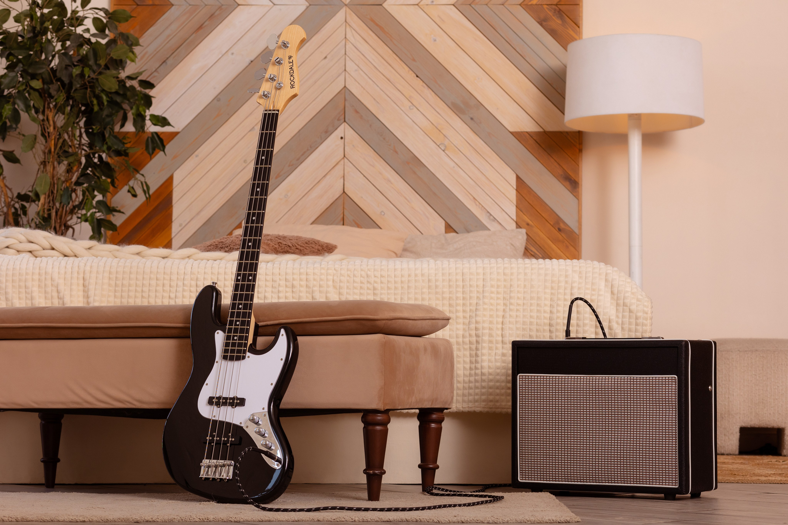 У банкетки стоит черно-белая гитара, подключенная к колонке.