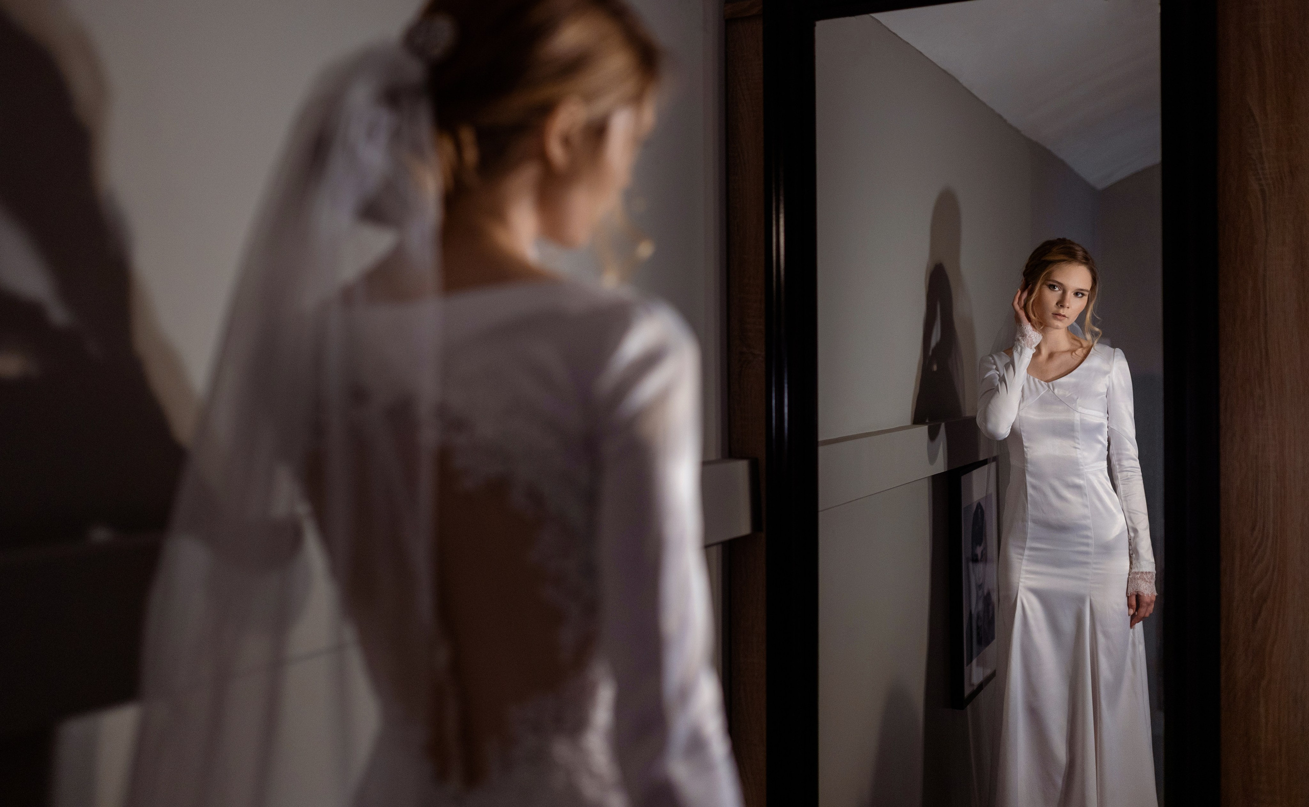 Невеста смотрит на себя в зеркало, поправляя прическу.