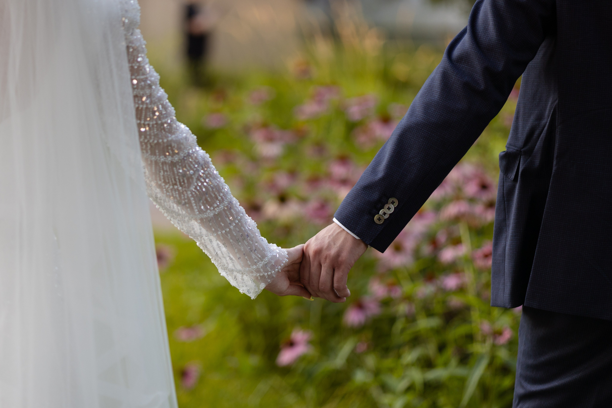 На переднем плане рука в руке молодых на фоне цветов.