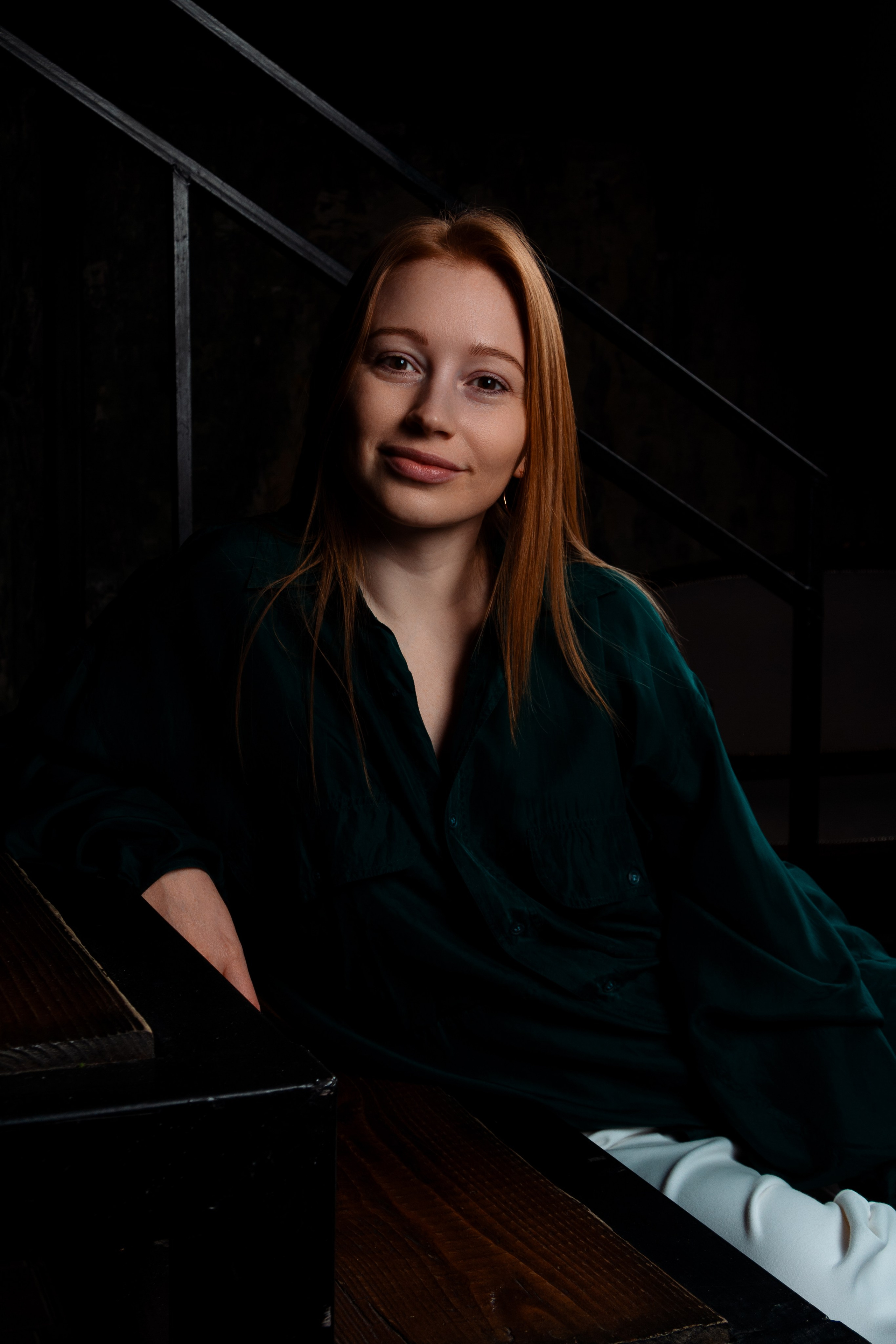 Рыжеволосая девушка сидит на ступенях в студии в зеленой рубашке