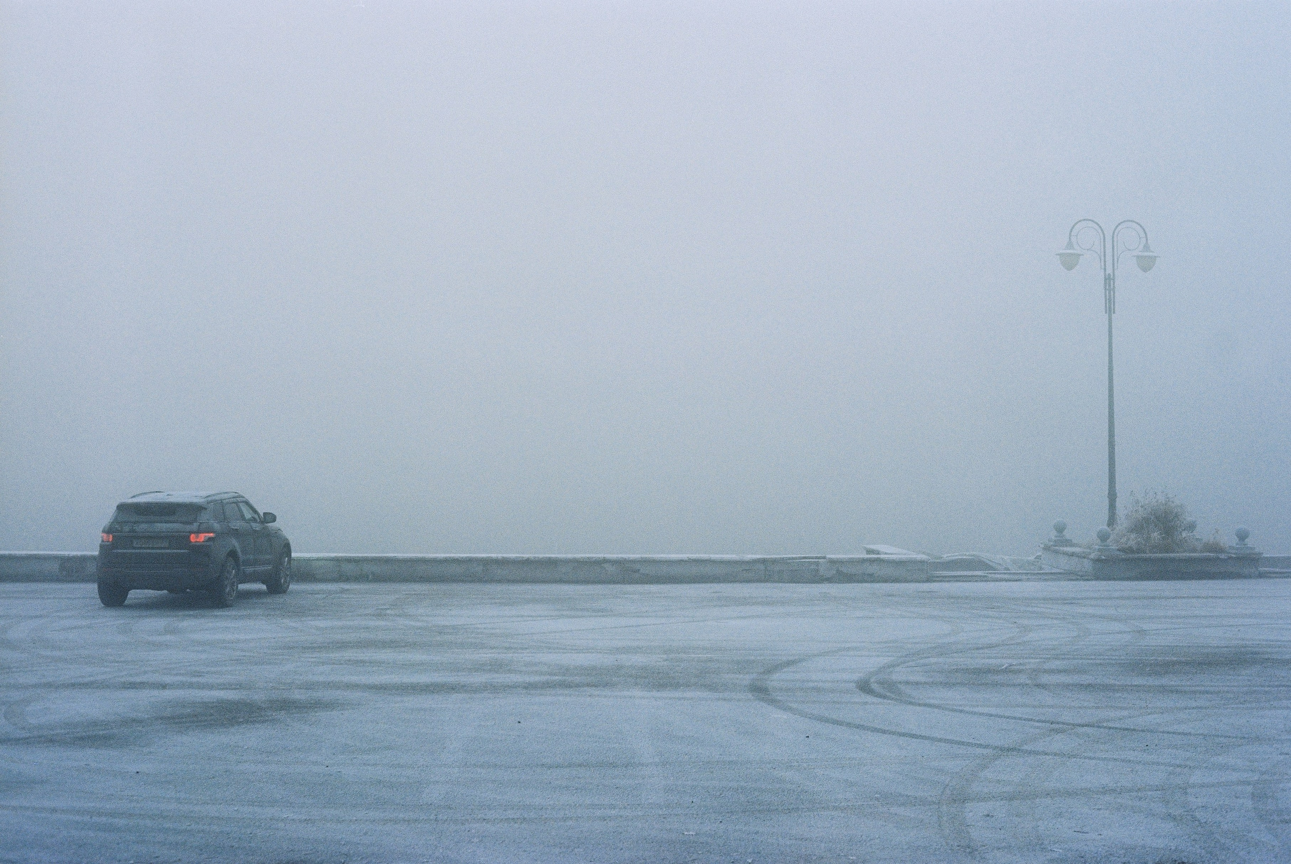 Постапокалиптический пейзаж, авто с зажженными фарами на фоне туманной пустоты.
