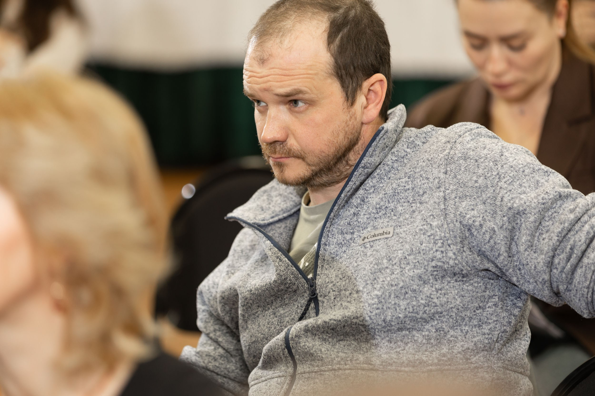 Мужчина в сером джемпере на стуле в зале сидит.