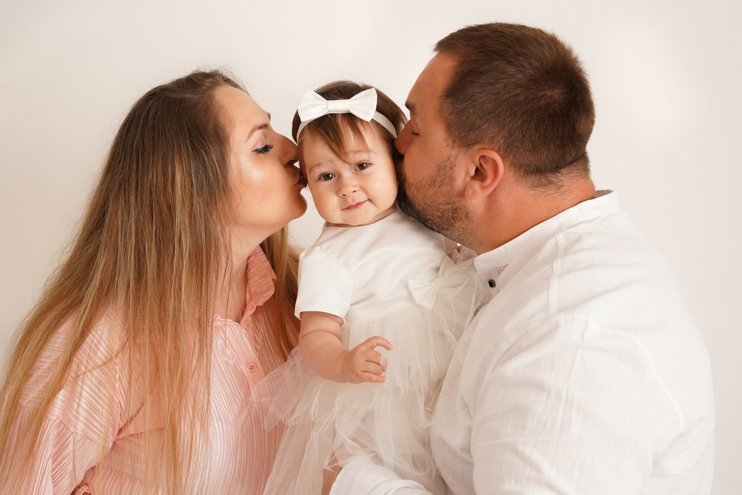 Папа и мама целуют дочку на фотосессии Первый год.