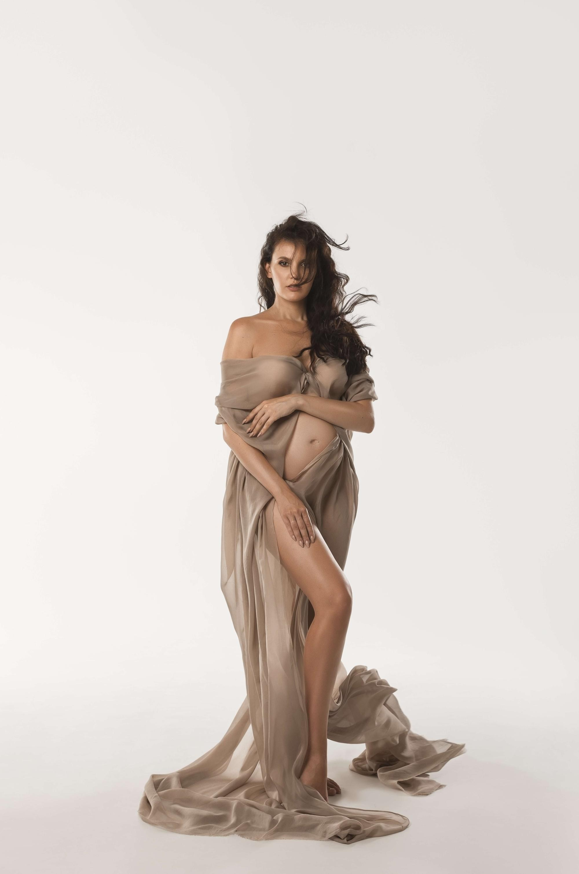 фотосессия беременной в фотостудии на светлом фоне в красивом разлетающемся платье, фотография беременности, фотосессия беременных, портрет беременной