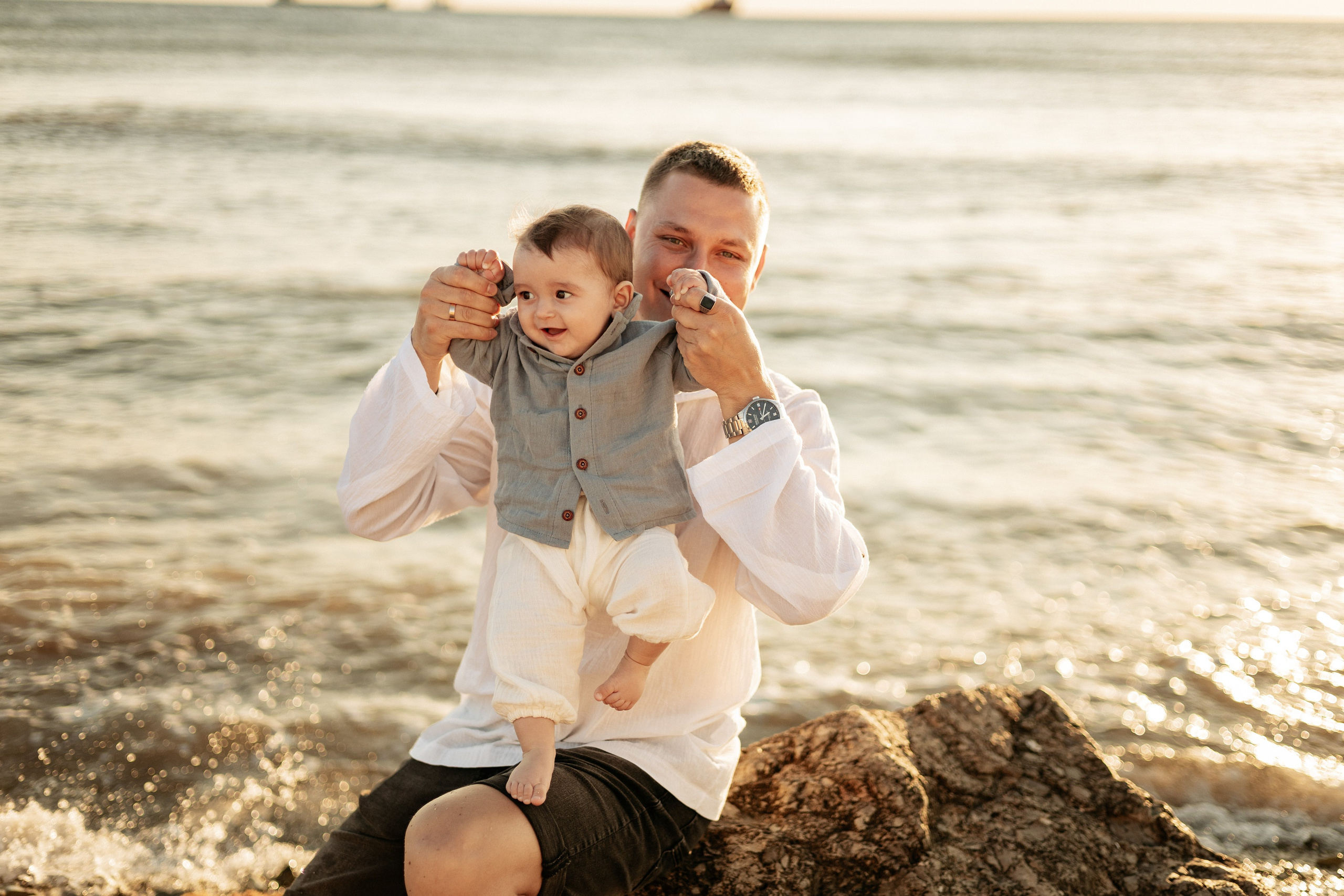 Папа держит сына на плечах на фоне моря и смеется