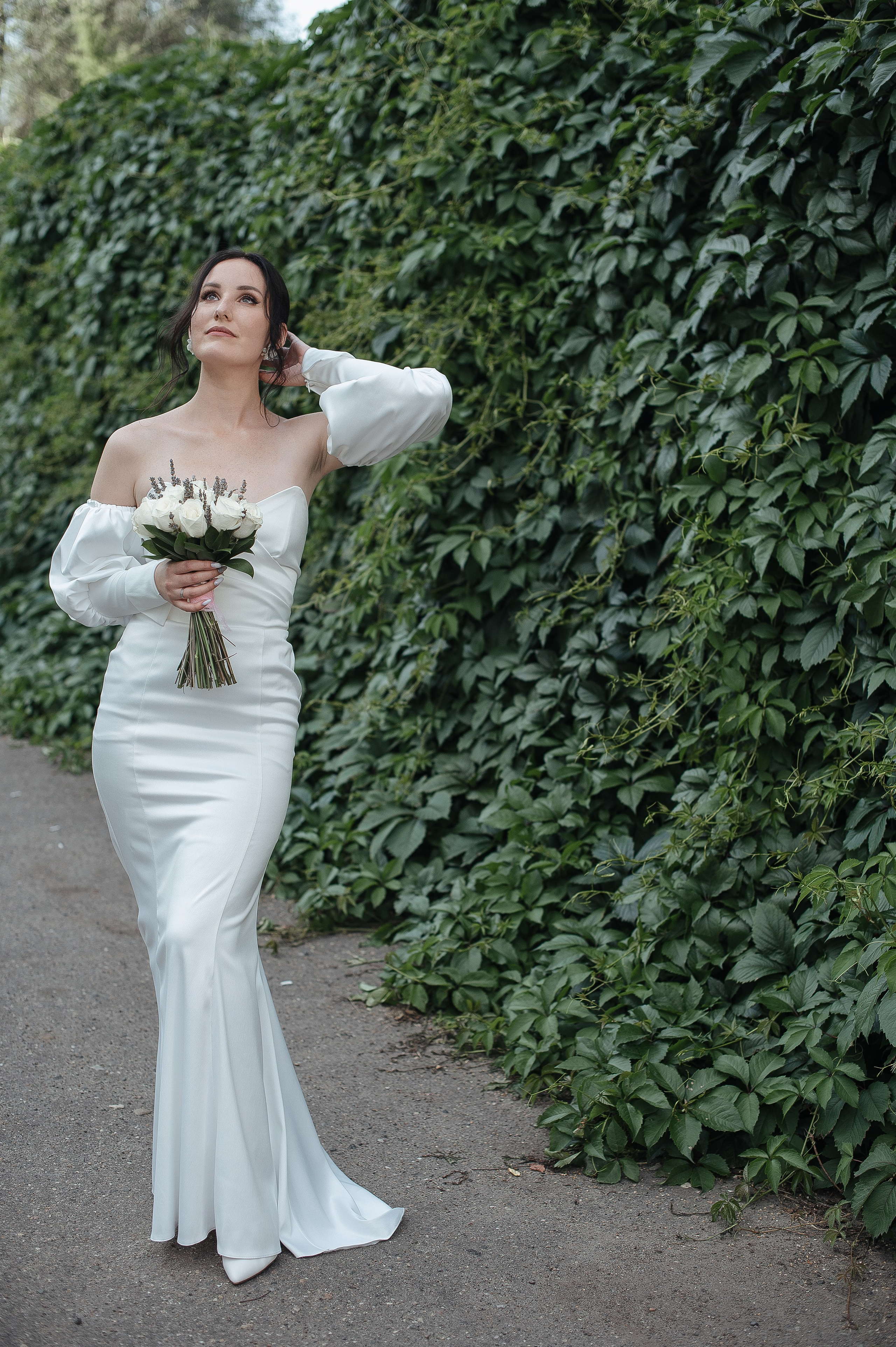 Невеста в полный рост в белоснежном платье с букетом в руках смотрящая вдаль