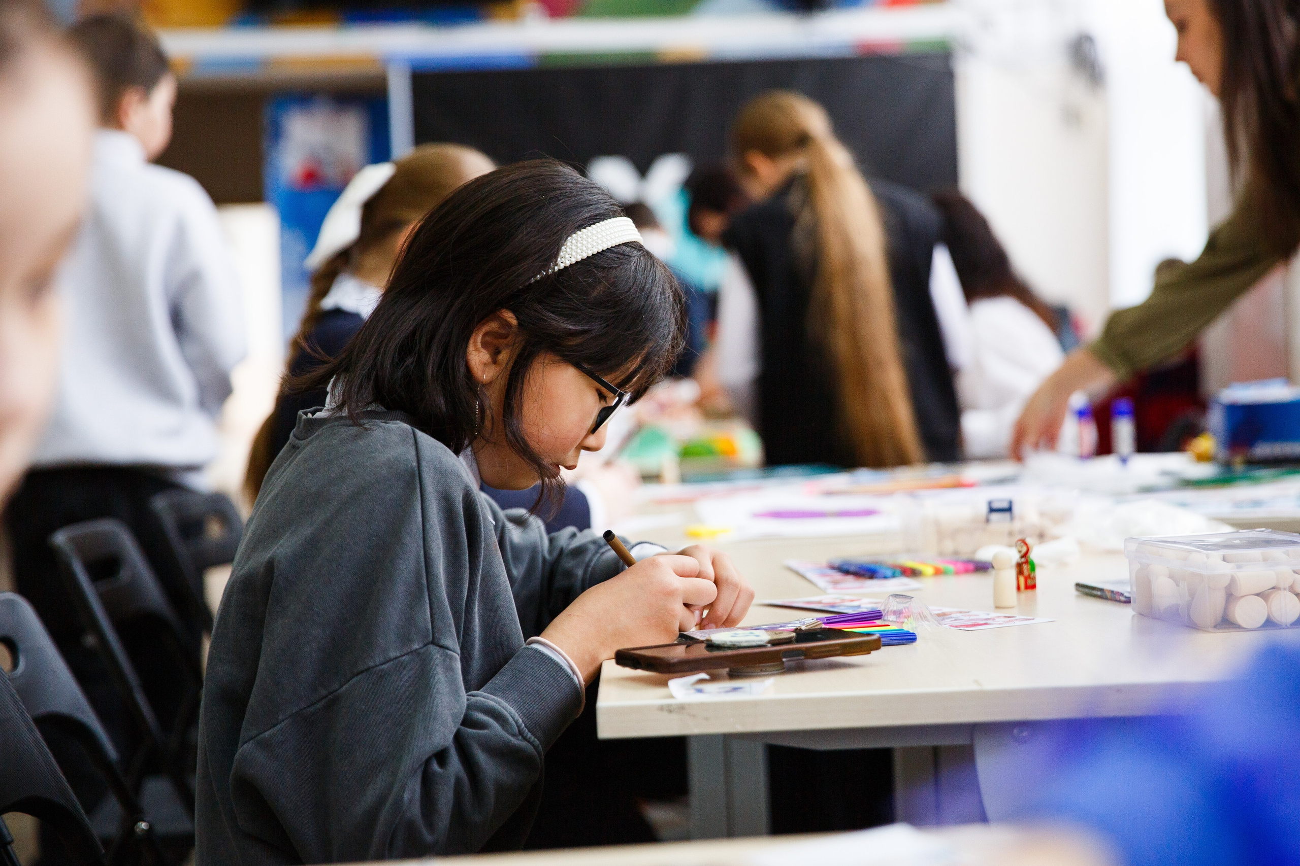 Девочка в очках рисует цветными карандашами.