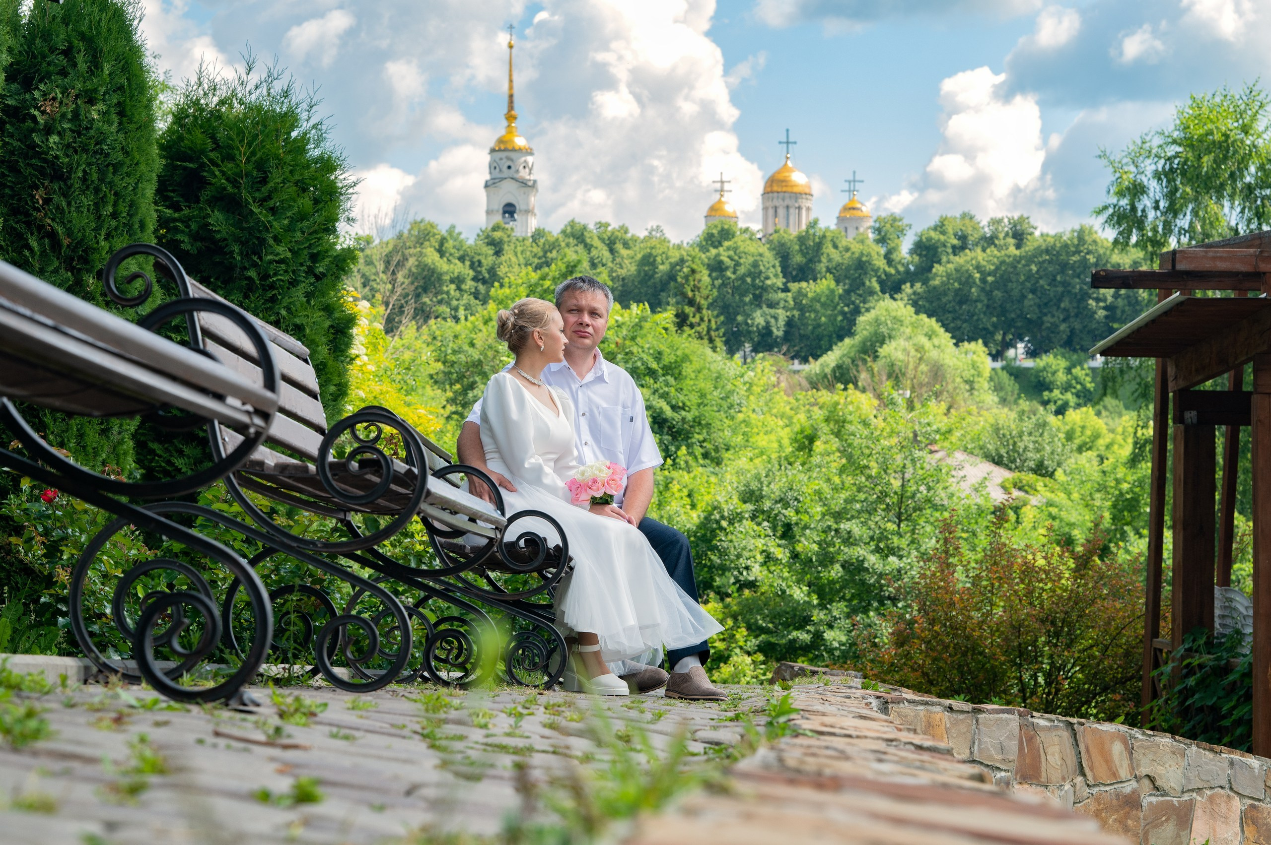 Прогулочная фотосессия после ЗАГСа на территории "Патриарших садов" во Владимире. Жених и невеста сидят на лавочке на фоне Успенского собора.