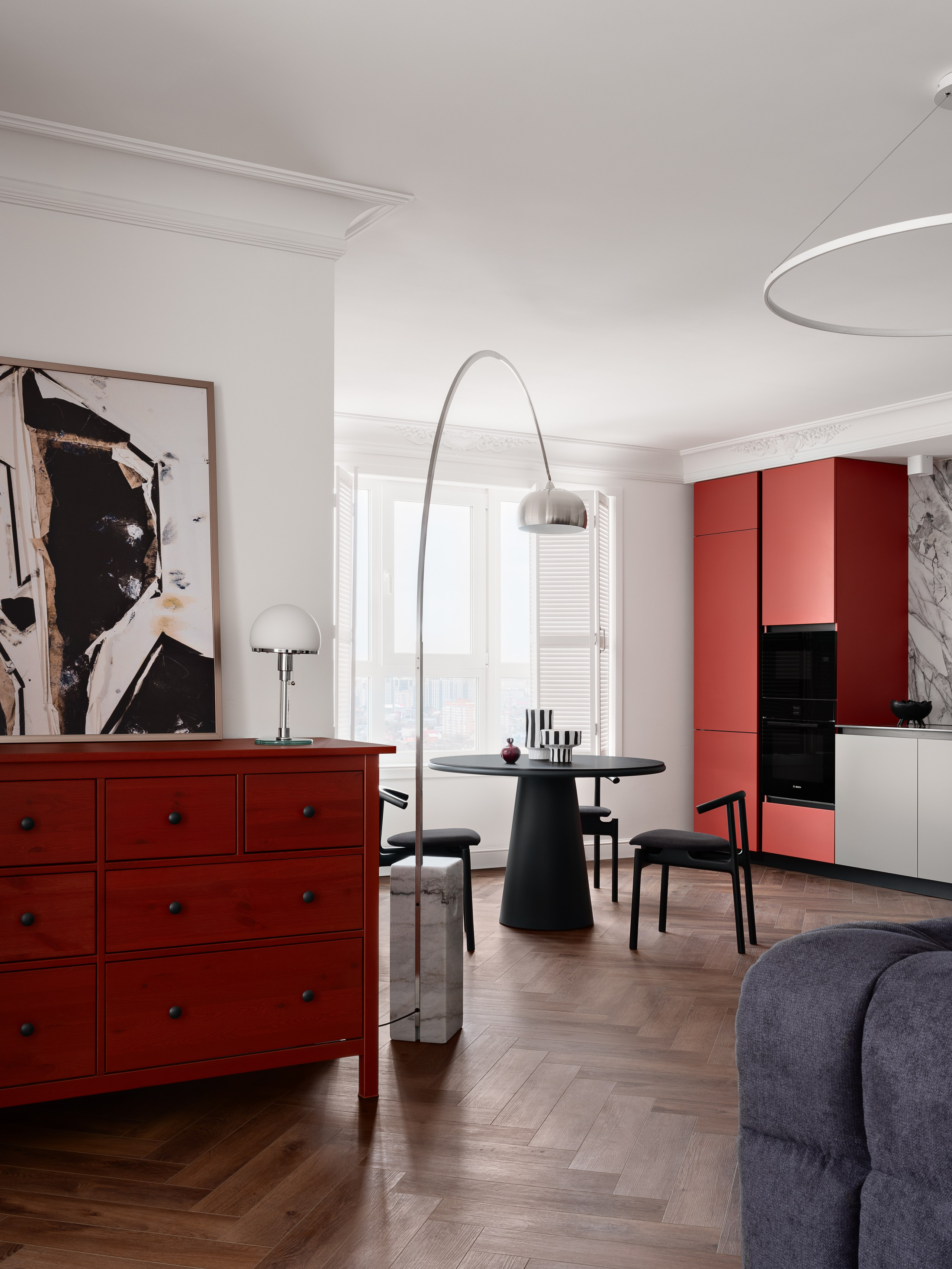 Современный интерьер кухни-гостиной с красным комодом, абстрактной картиной и круглым черным столом в центре. Минимализм и стиль подчёркивают дизайн от Антона Логинова, стилизацию Алёны Мощенской и фото Сергея Денисенко.