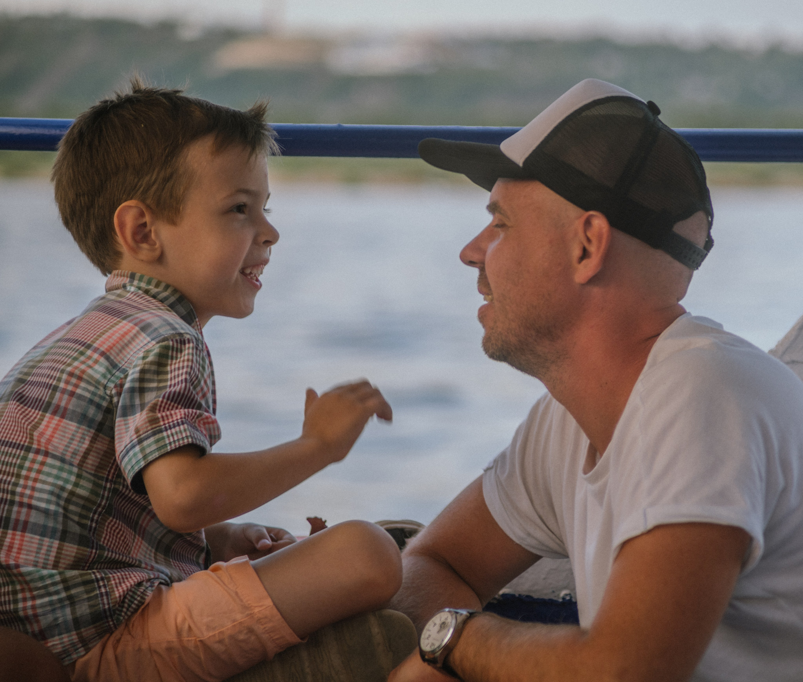 Мальчик и его отец с улыбками смотрят друг на друга во время прогулки на лодке — момент радости и семейного единства.