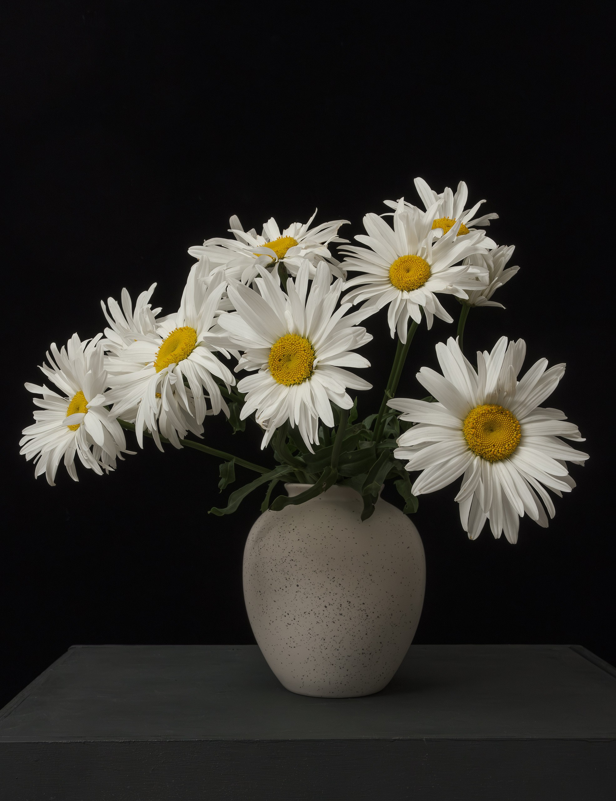 Букет ромашек в вазе на черном фоне.