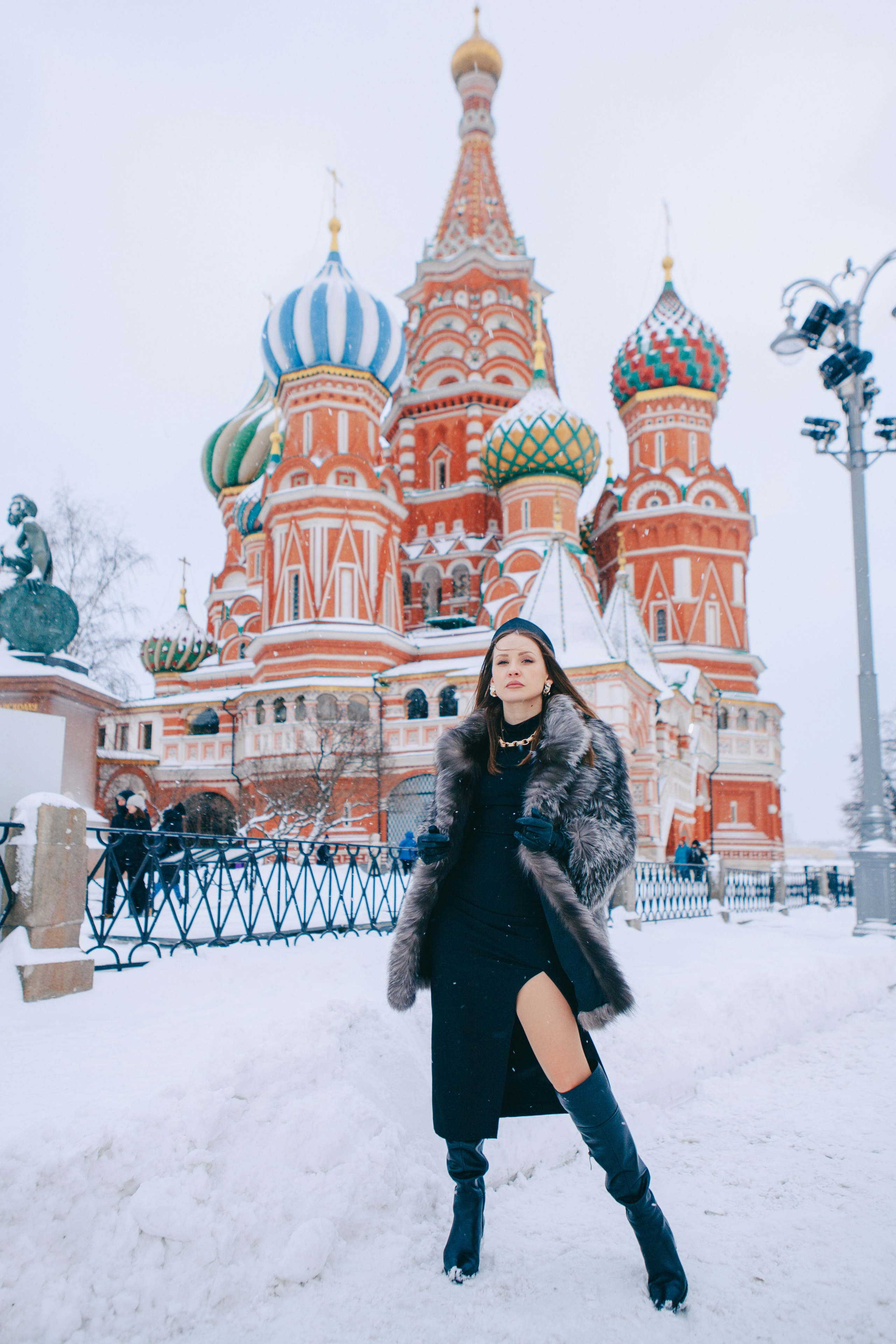 Девушка позирует в кокошнике, высоких сапогах и в черном платье с разрезом на фоне Храма Василия Блаженного. Главная достопримечательность в центре Москвы