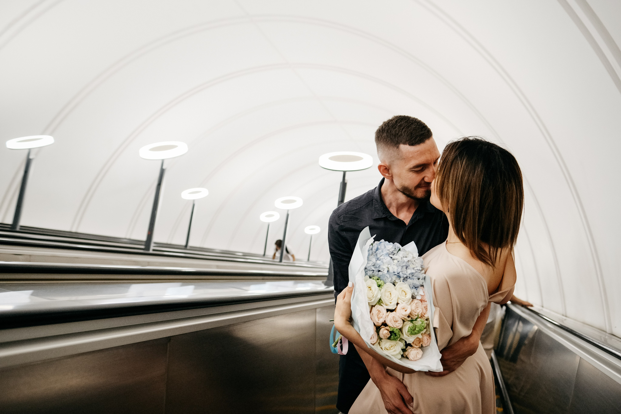 Влюбленные с букетом спускаются на эскалаторе в метро.