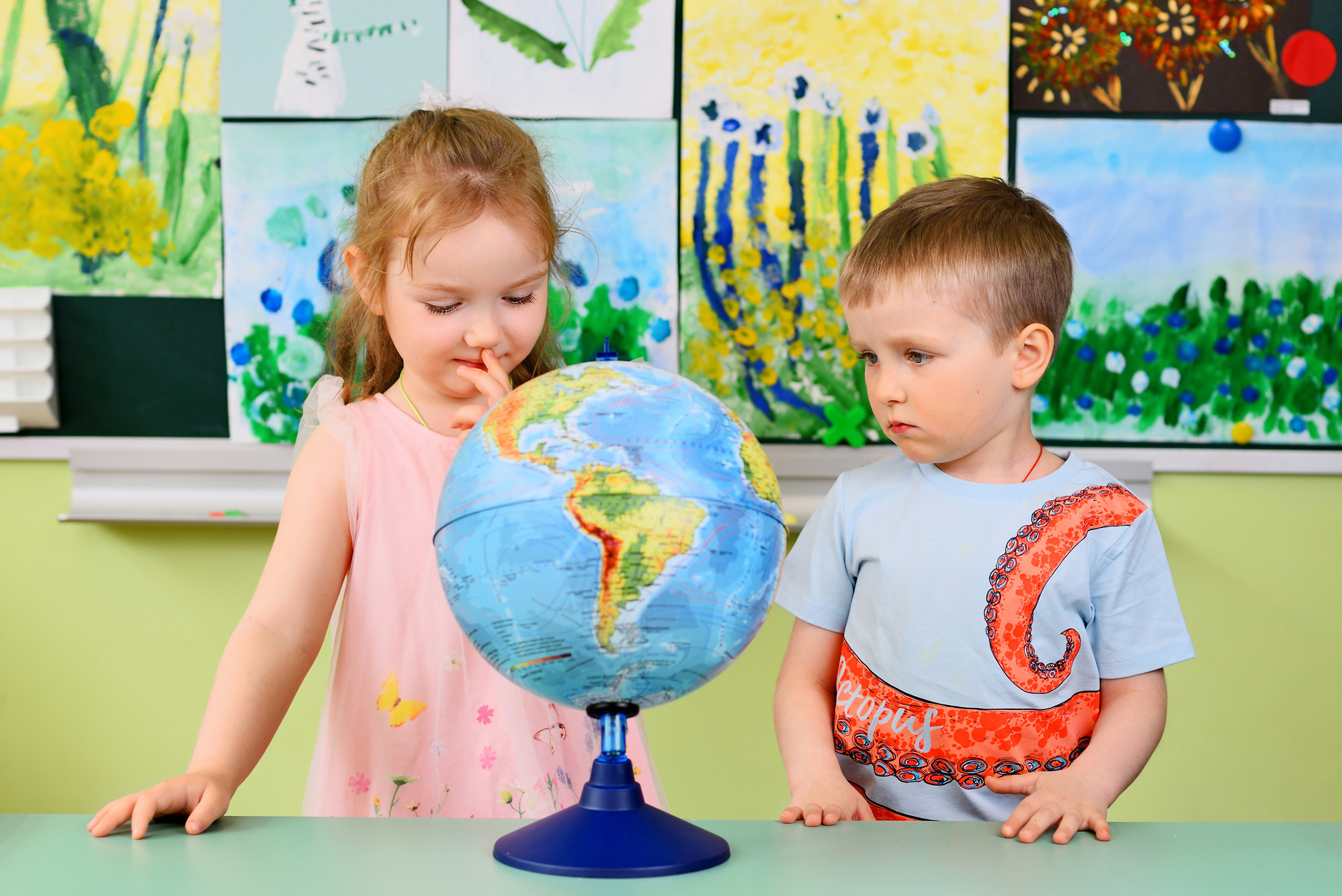 Девочка и мальчик в детском саду изучают глобус.