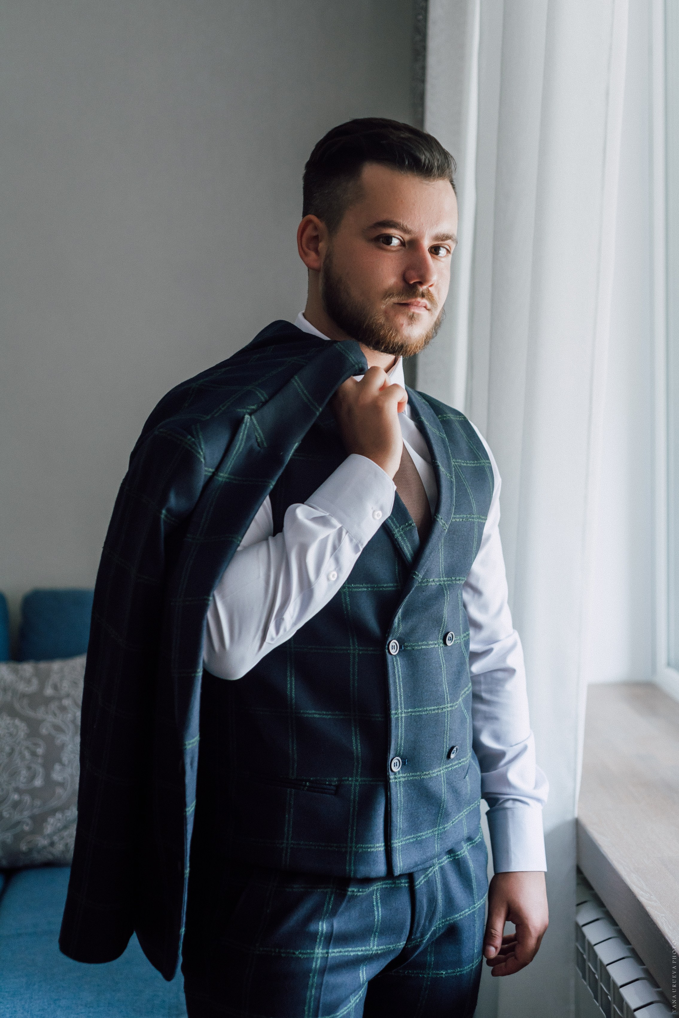 Жених в темно-синем костюме стоит у окна