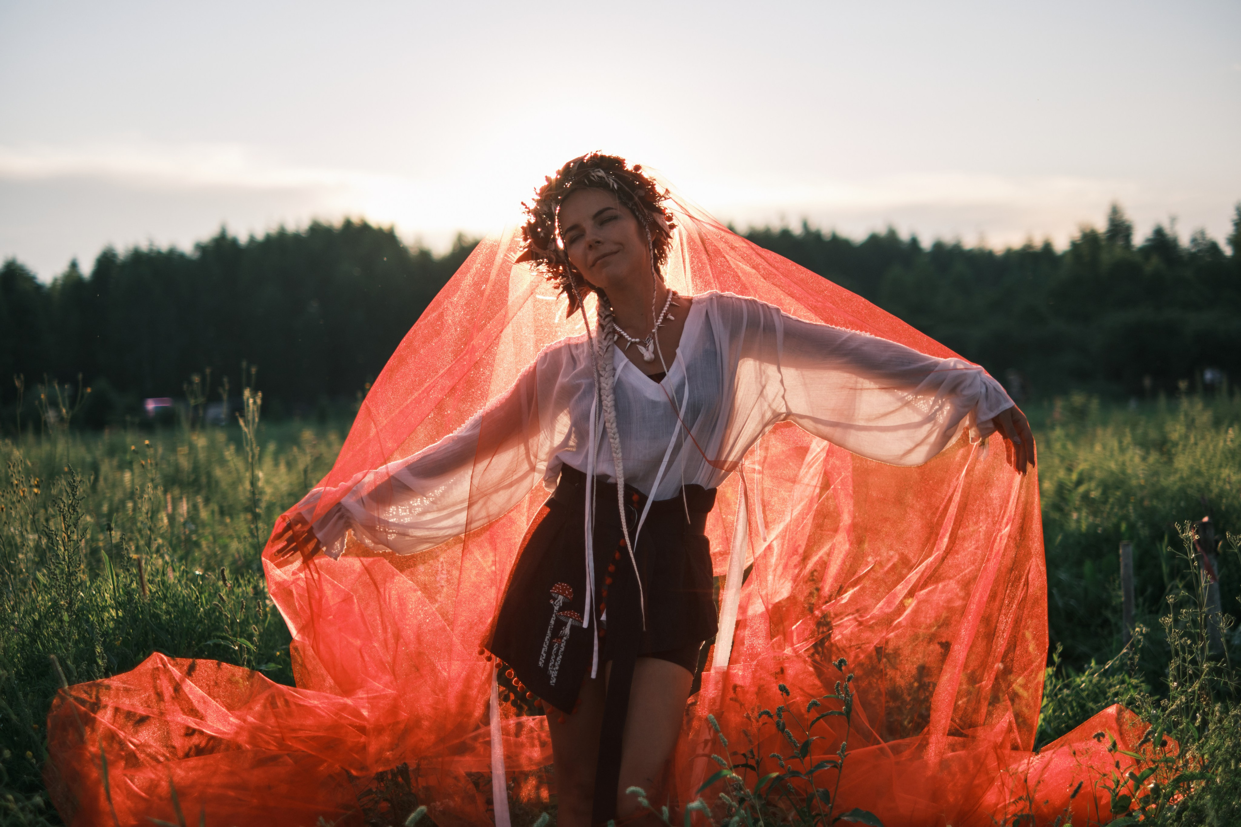 Девушка с красной тюлью стоит на фоне заката