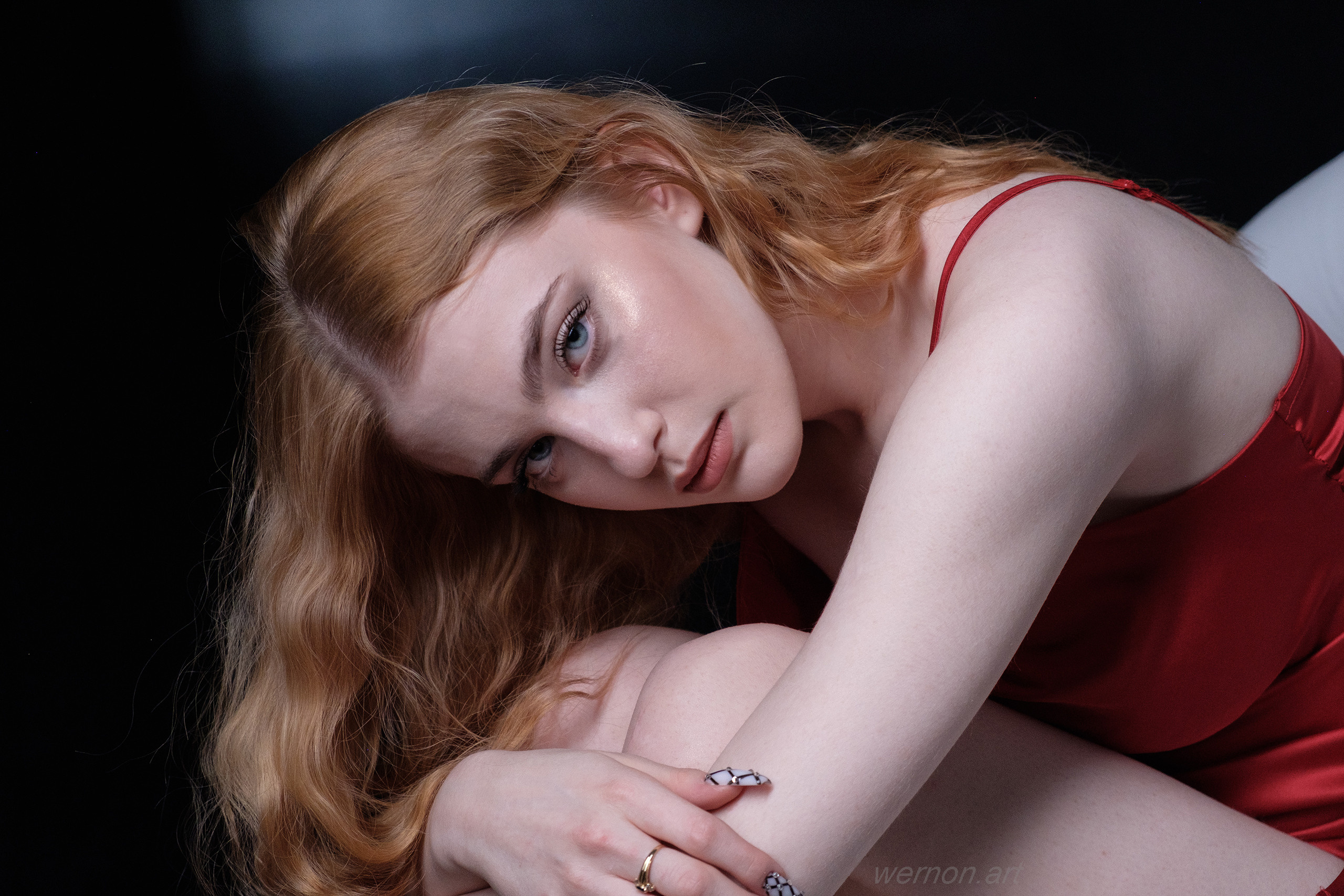 Девушка в красном платье сидит в кресле, склонив голову и смотрит в камеру.