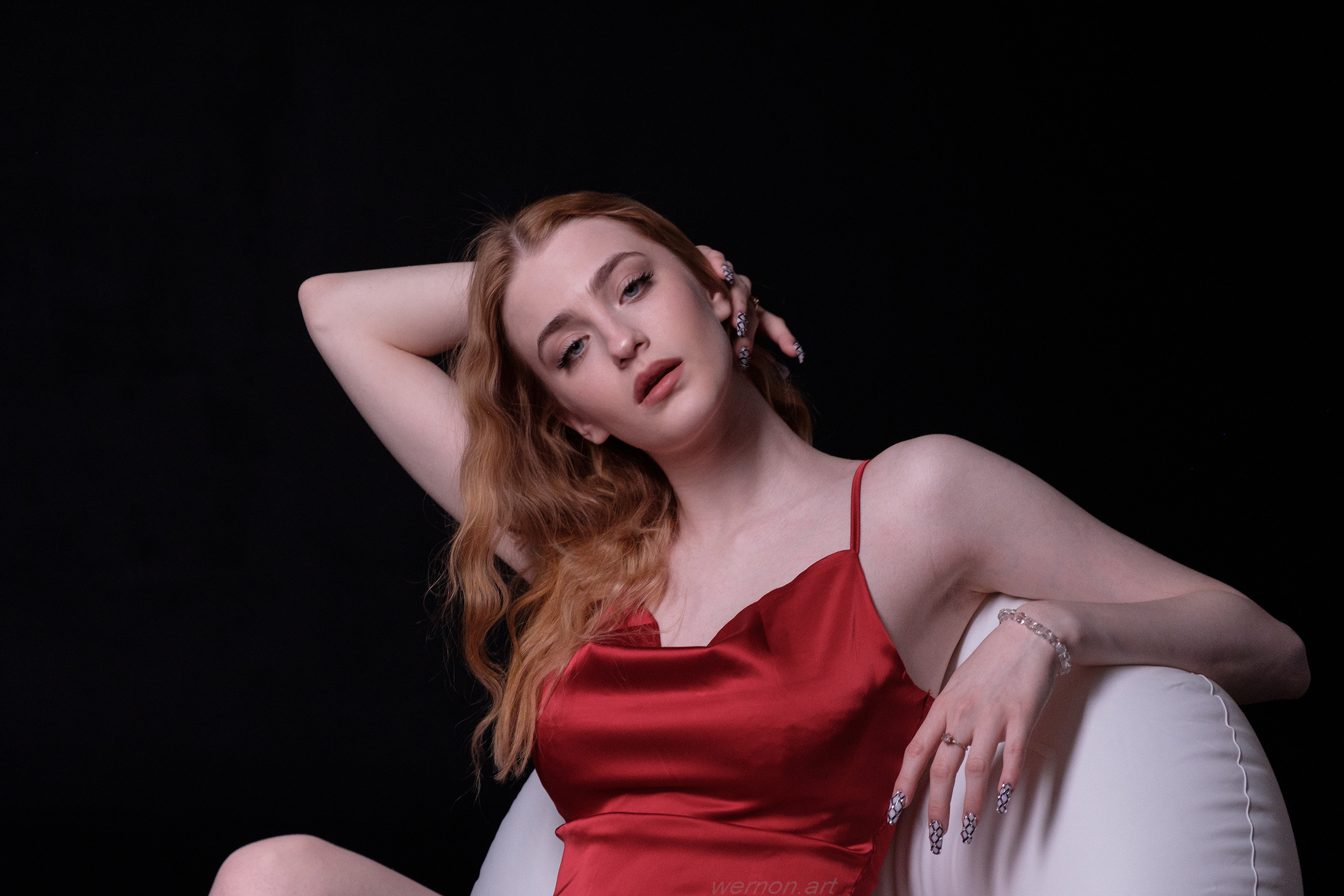 Девушка блондинка в красном платье сидит в кресле,закинув руку за голову.