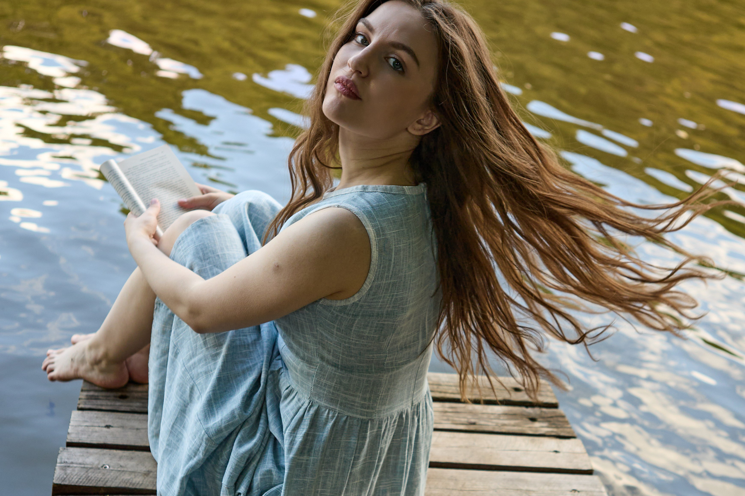 девушка с развевающимися волосами на пирсе у реки
