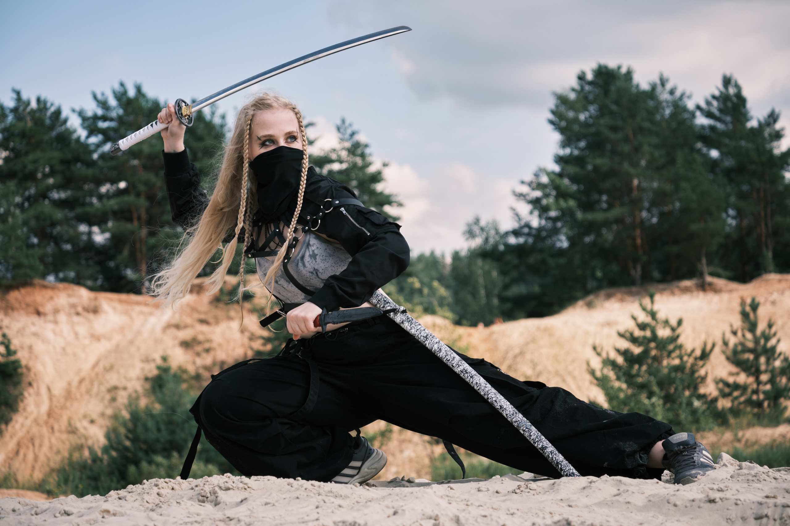 Светловолосая девушка с катаной в руке и черной маске на лице стоит в боевой стойке