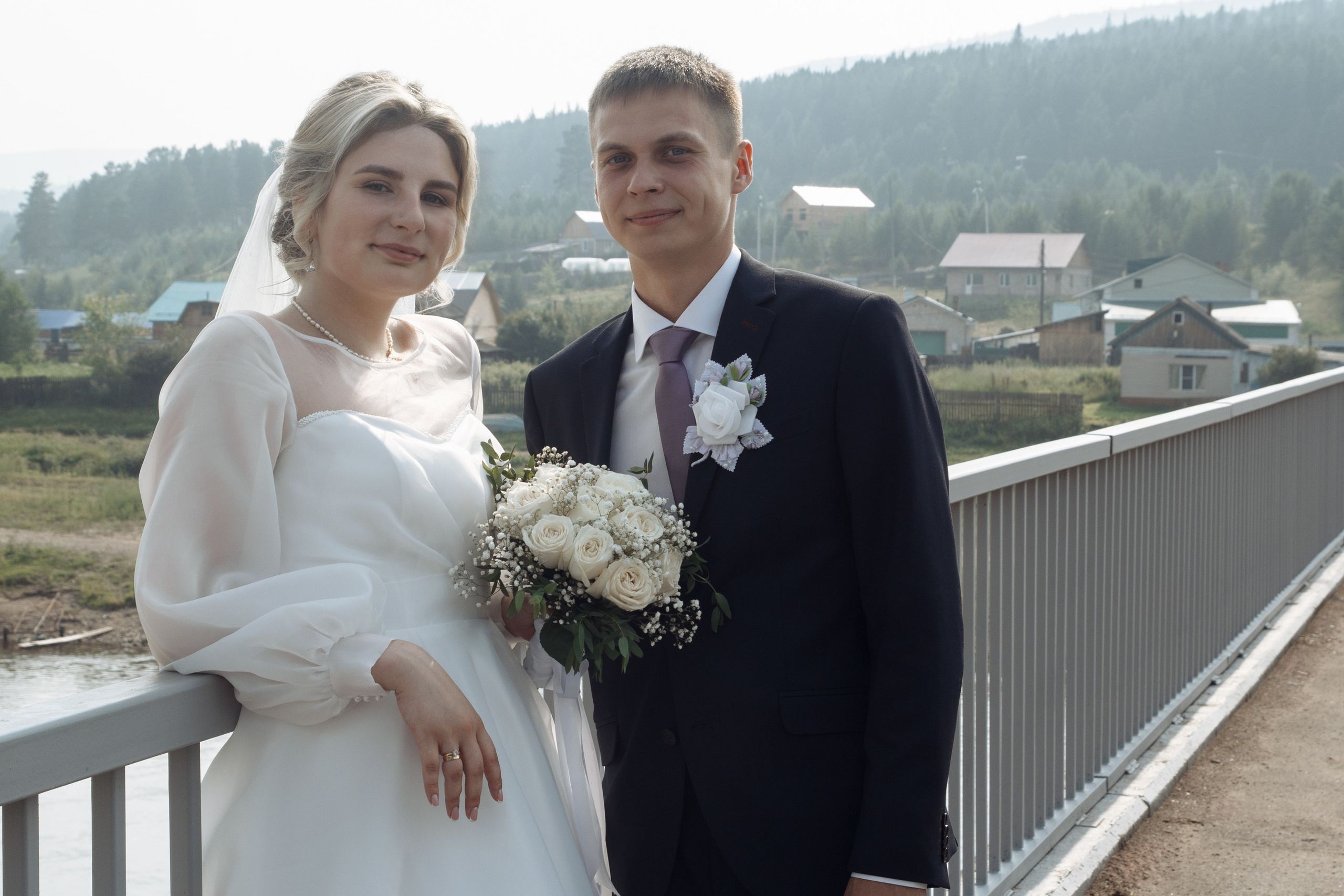 Портрет жениха и невесты на фоне деревенского пейзажа, невеста с букетом в руках.