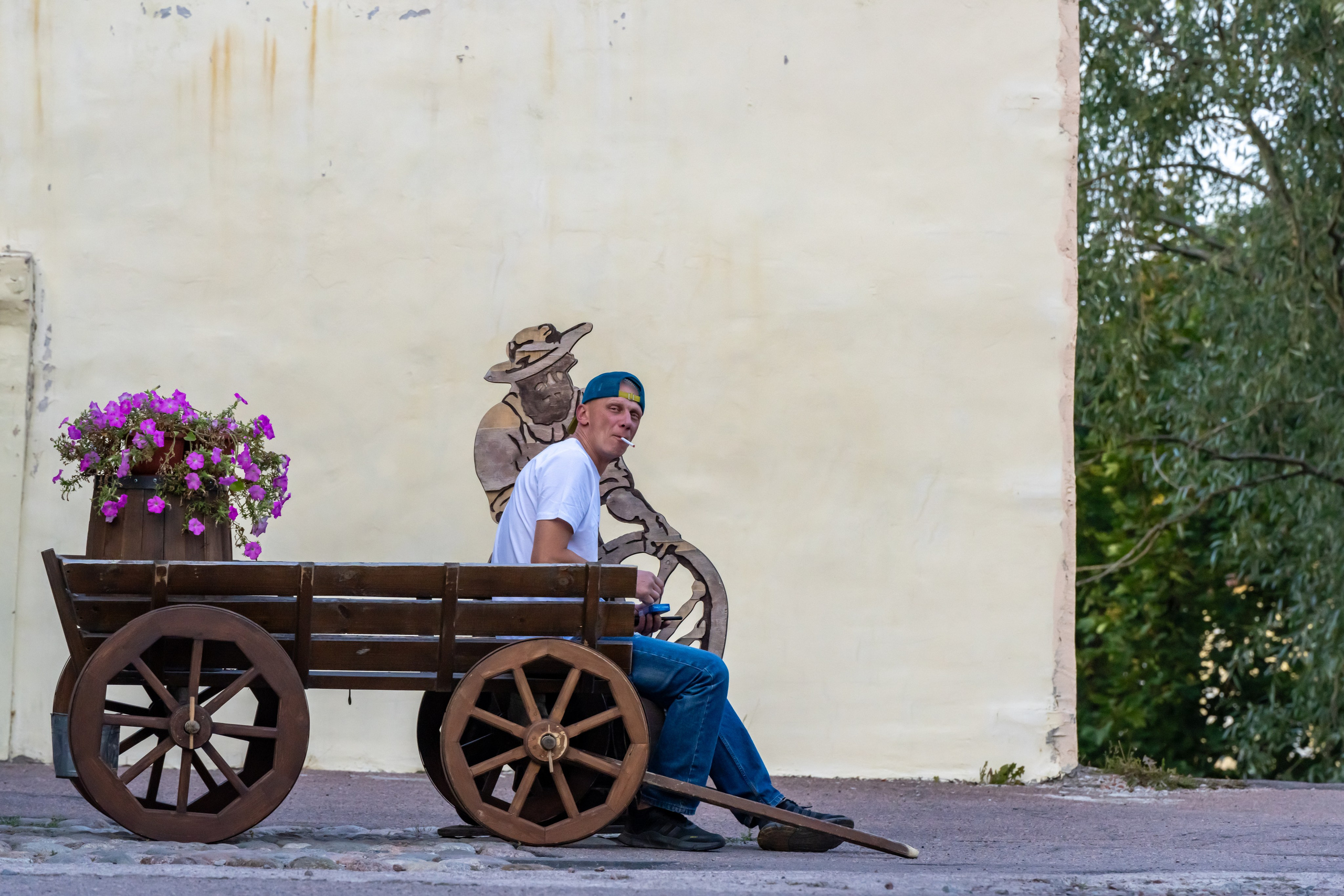 Мужчина сидит на телеге и курит, а изображение на стене на него смотрит