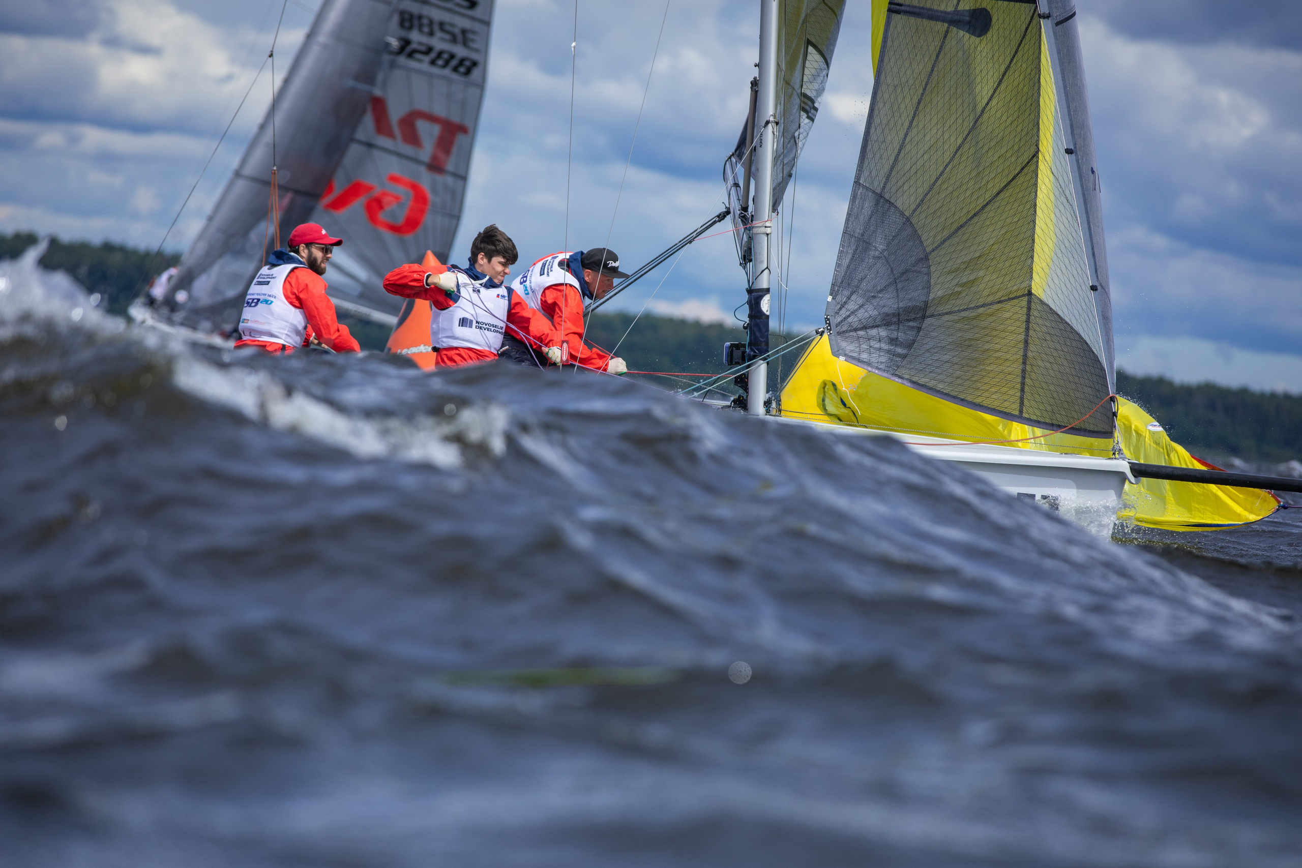 Волна накрывает спортивную парусную яхту. Постановка генакера на регате.