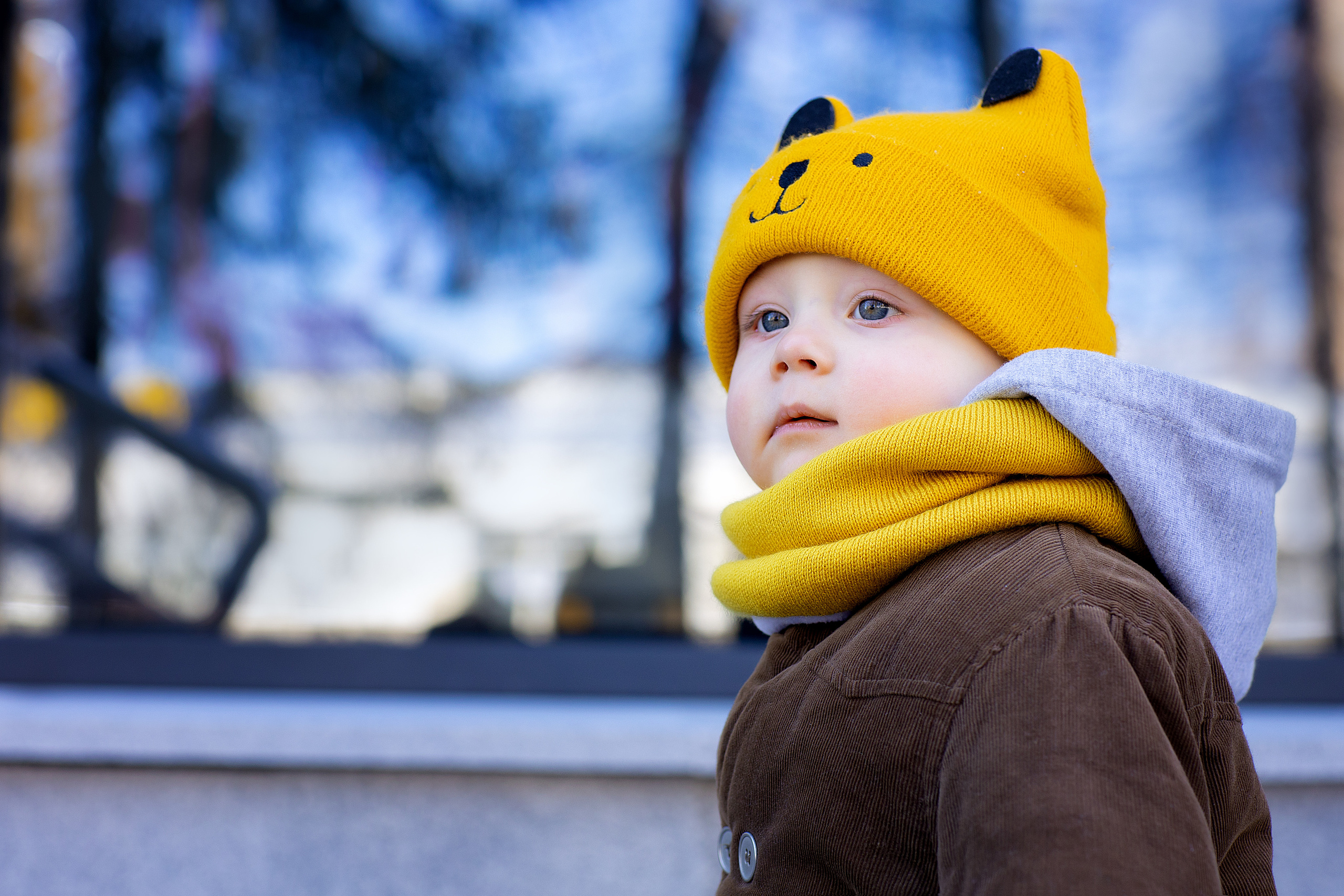 Мальчик в желтой шапке на фоне витрин магазинов