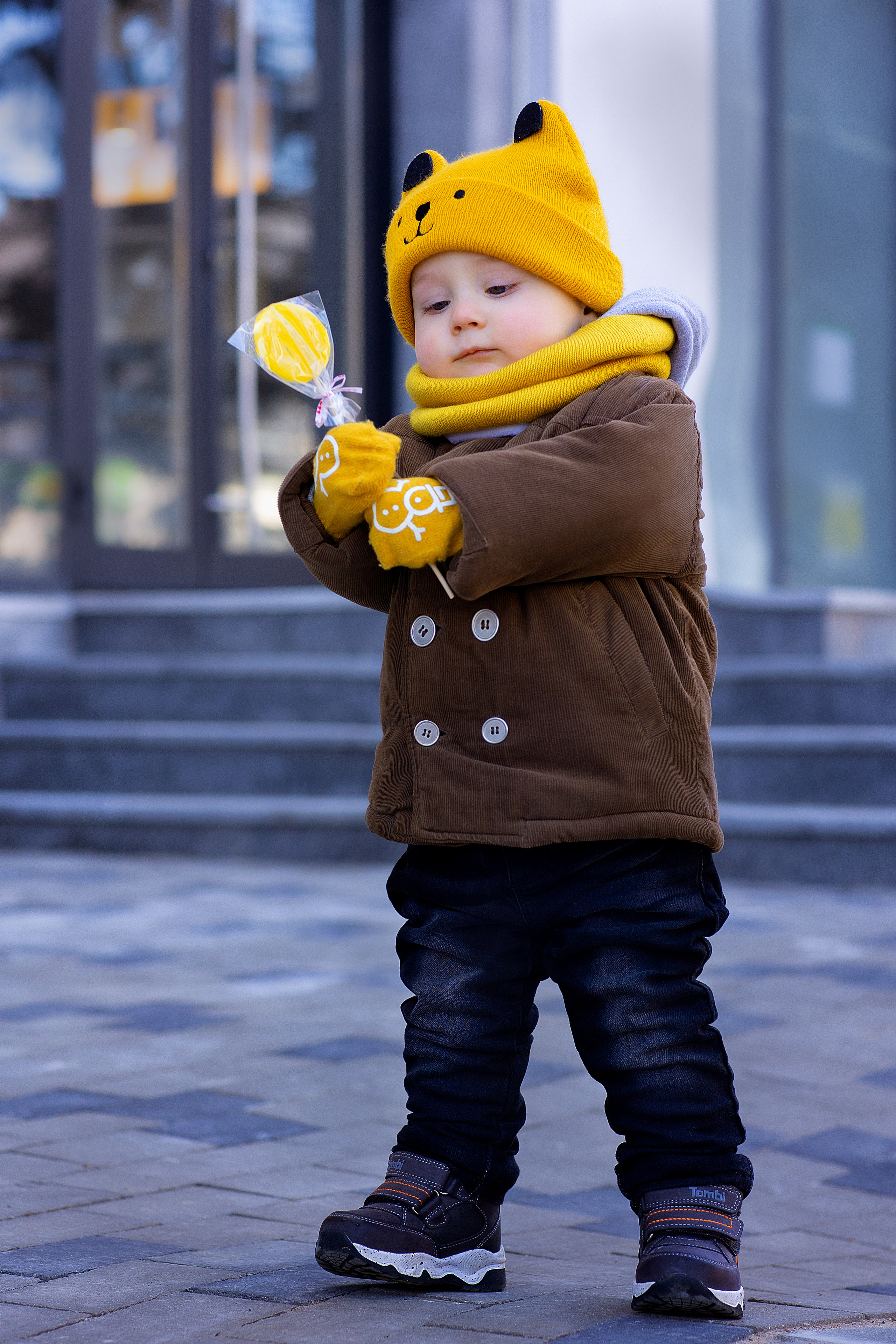 Мальчик в желтой шапке с леденцом в руках