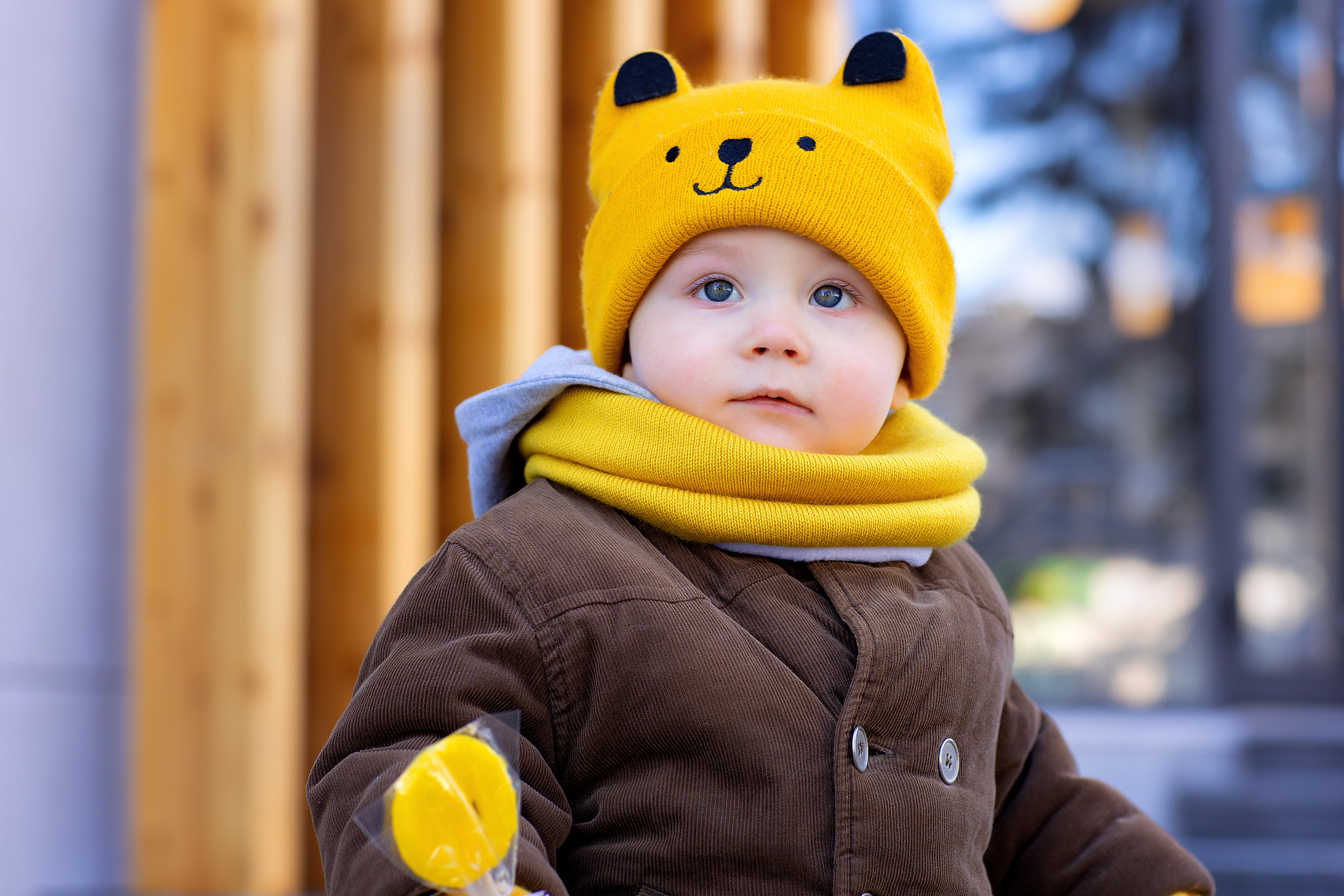 Мальчик в желтой шапке гуляет на фоне витрин магазинов ранней весной