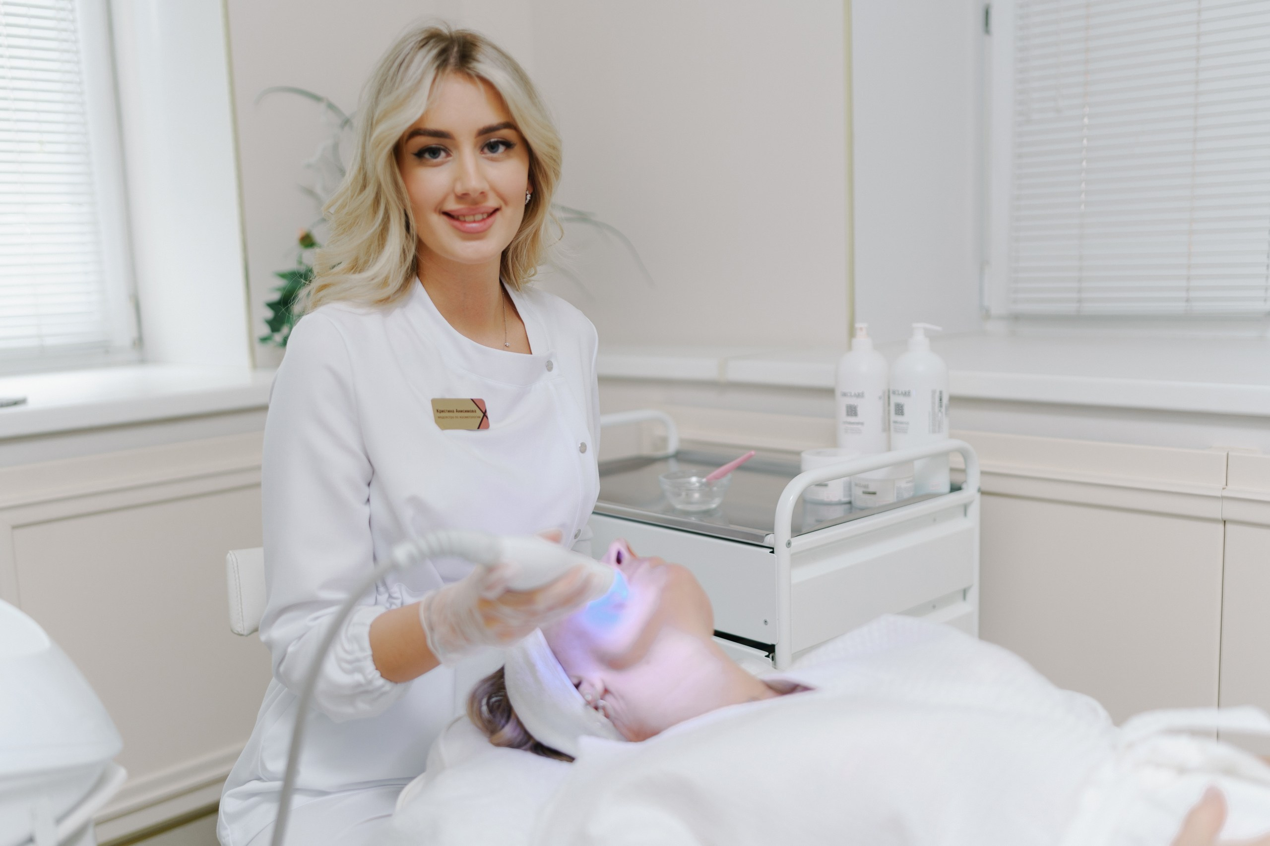 девушка на сеансе анти эйдж медицины во время процедуры смотрит в камеру и улыбается