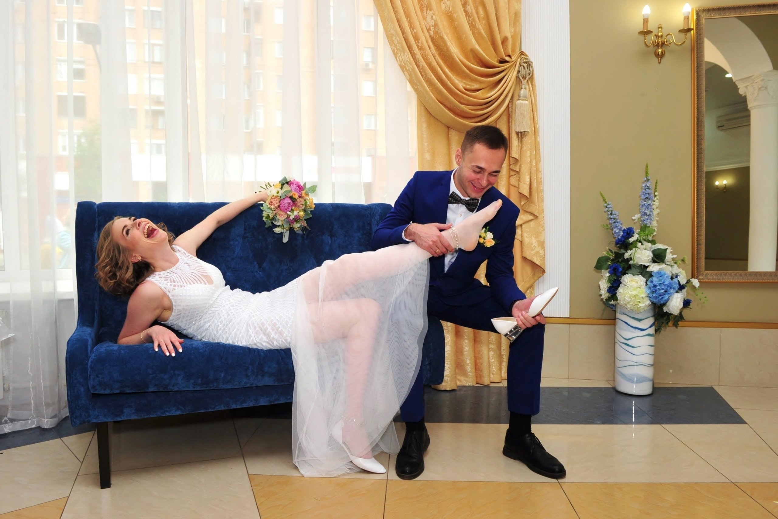 В Таганском ЗАГСе, жених надевает туфельку на ногу невесте, невеста лежит на синем диване и хохочет