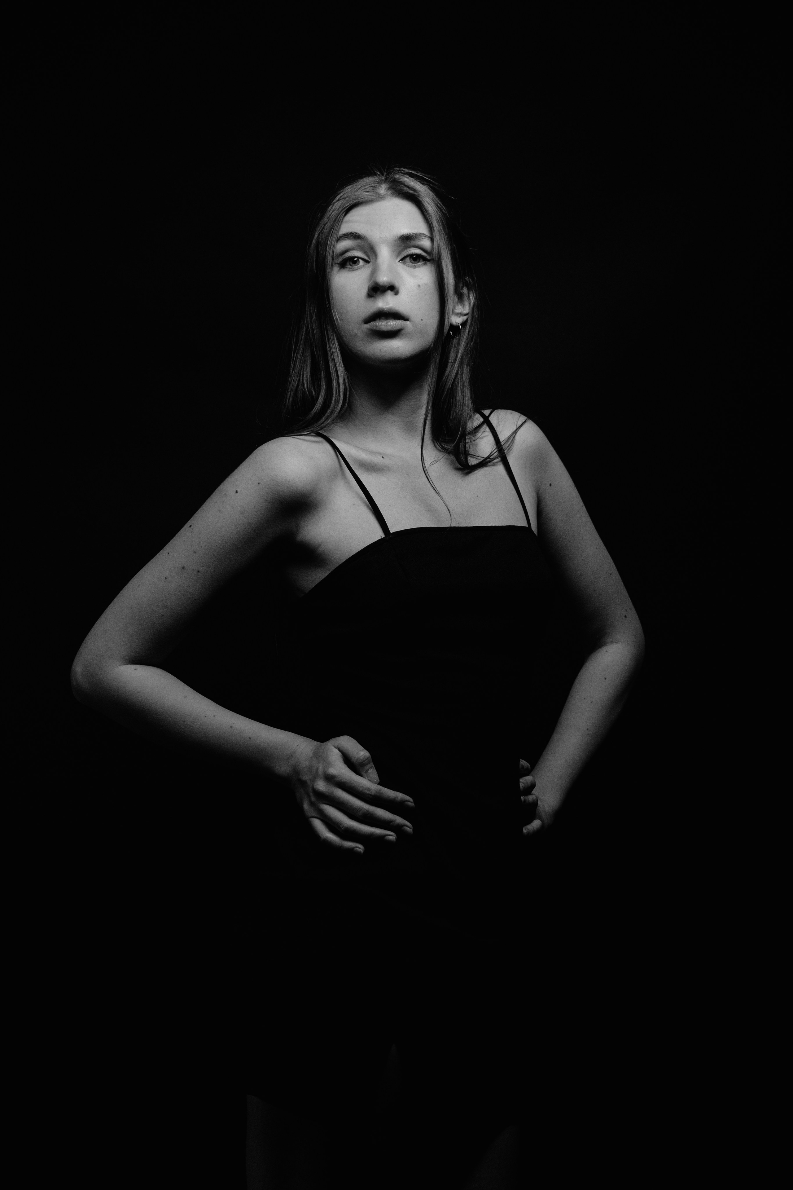 Модель в чёрном платье на чёрном фоне позирует