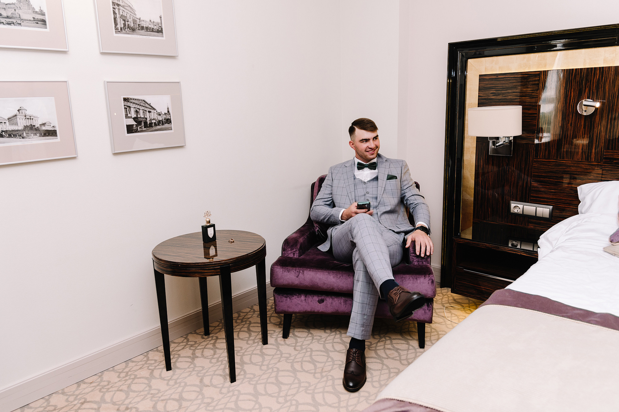 Жених ждет свою невесту сидя на красном кресле в отеле.