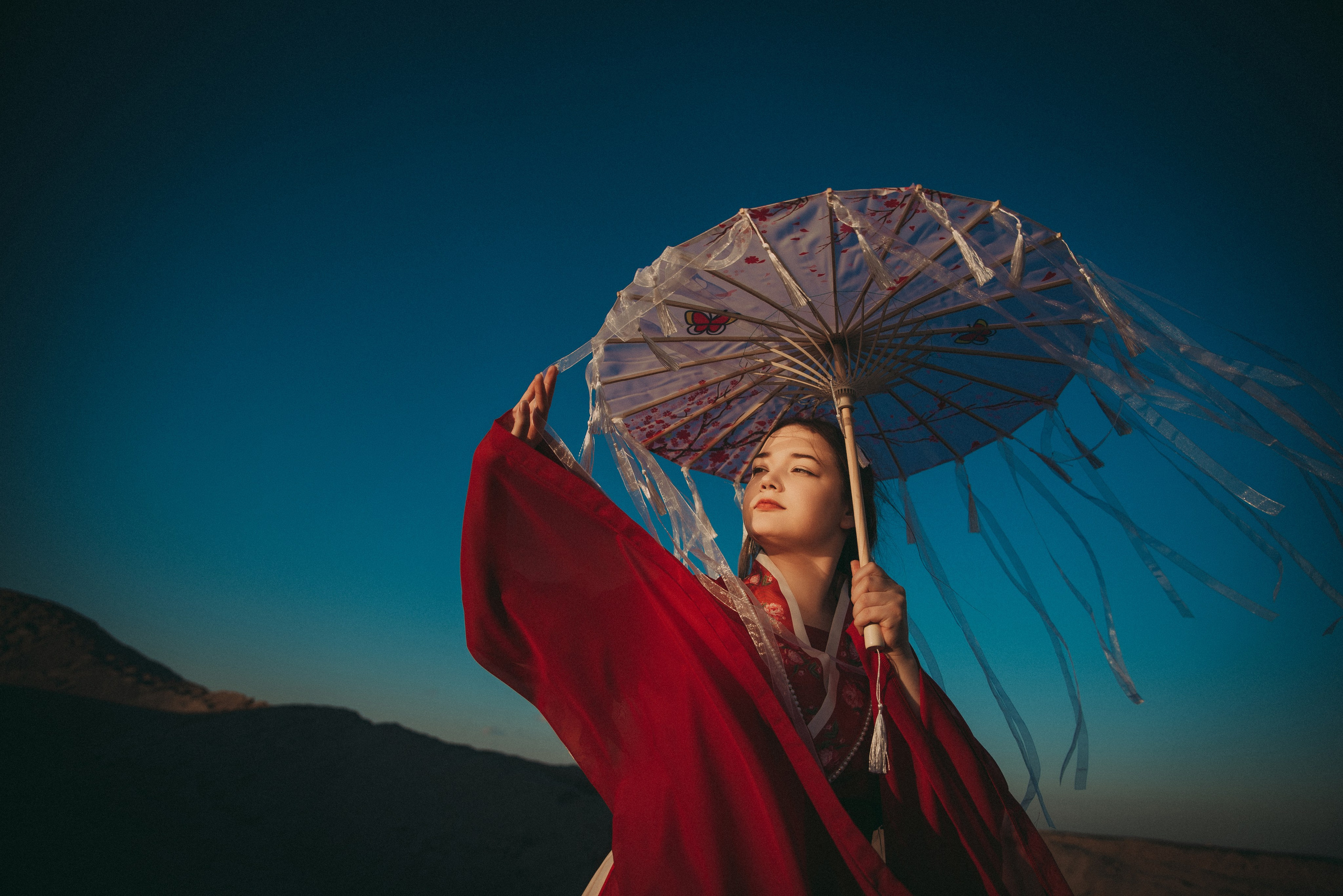 девушка в песках под зонтом смотрит на солнце