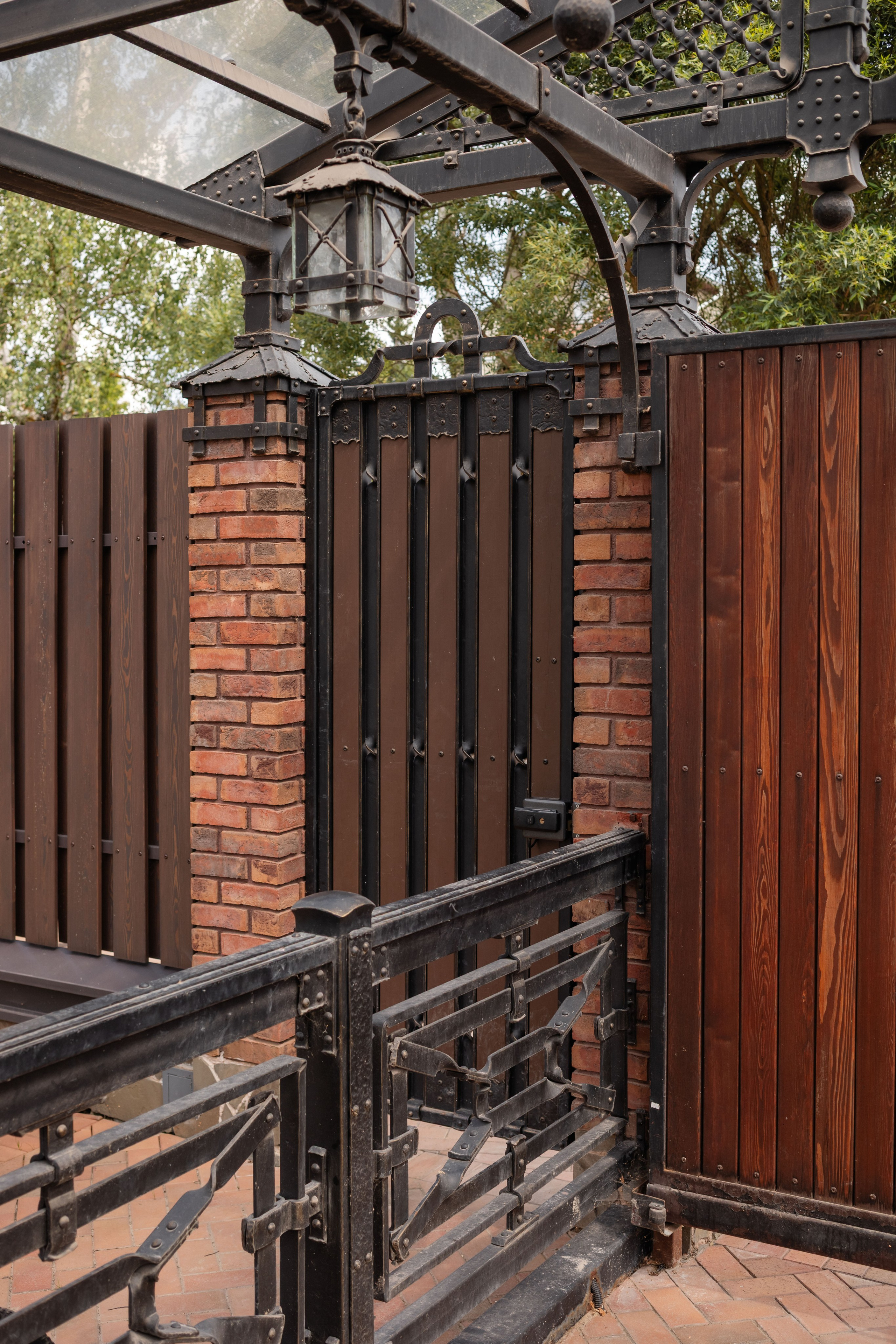 Забор в стиле Лофт — тёмные вертикальные планки, кирпичные столбы и металлические элементы. Единый стиль с гаражом.