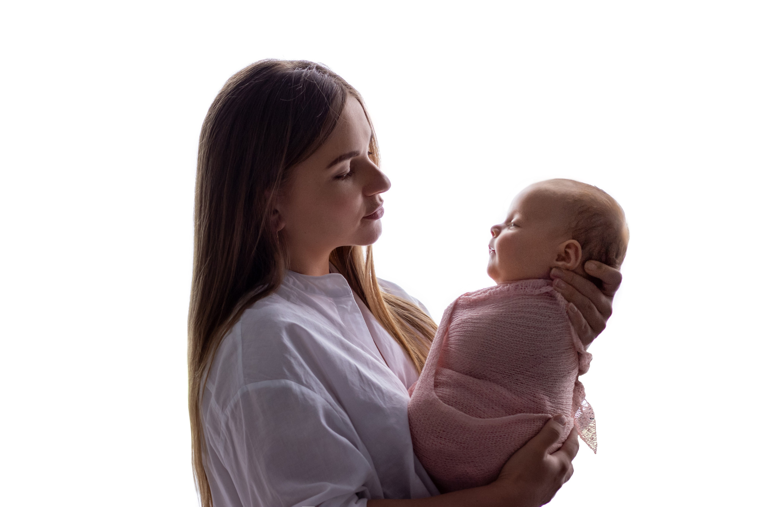 портрет - молодая мама стоит в белой рубашке на белом, держит новорожденную дочь в розовой обмотке и нежно смотрит с любовью
