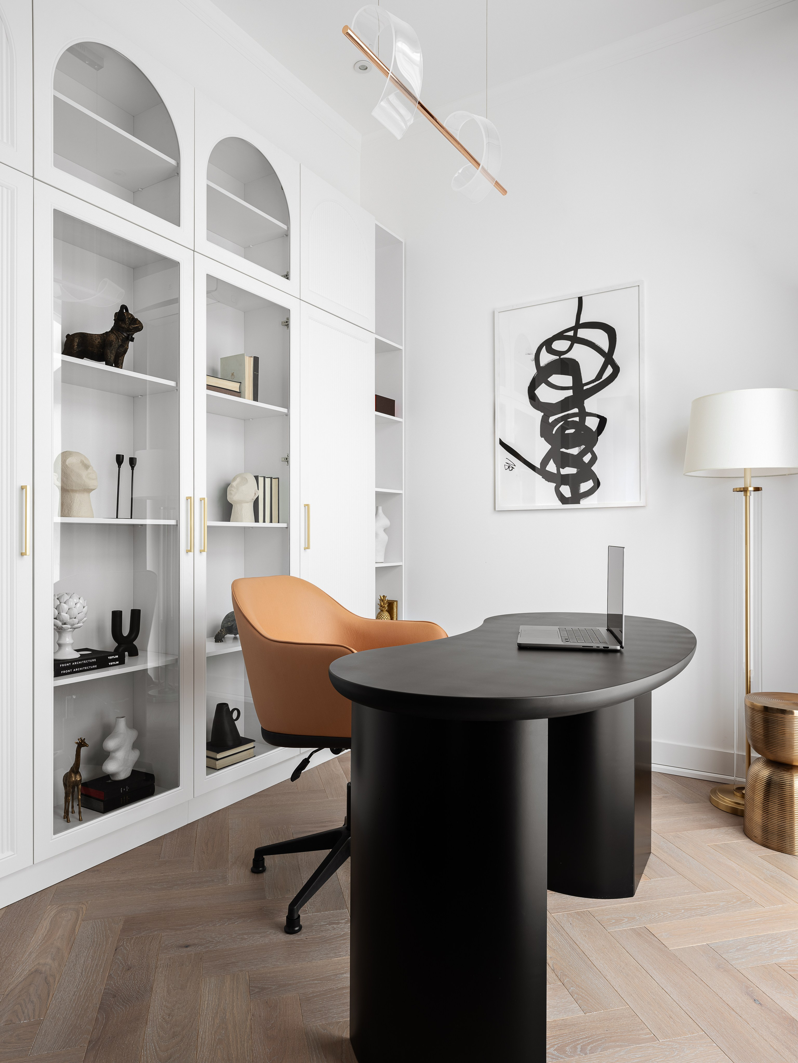 Кабинет с современным дизайном интерьера: чёрный овальный письменный стол, кресло цвета карамели, встроенный белый шкаф с арочными фасадами и декоративными скульптурами. Проект оформлен дизайнером Василиссой Бачевой, стилист Наталья Якушева, фото Сергей Денисенко.
