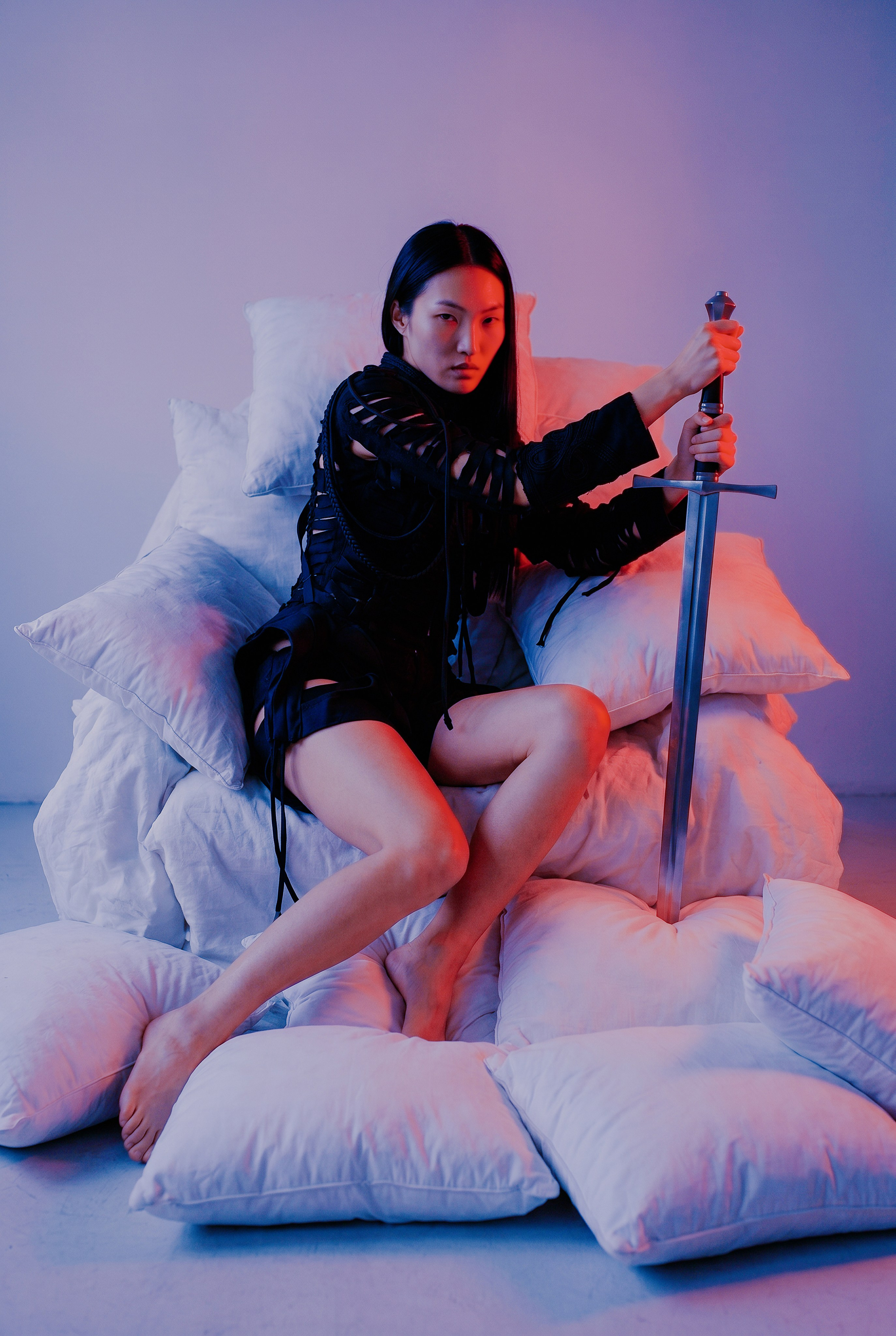 Арт‑кадр с метафорой силы и уязвимости: собранный взгляд модели и уверенная хватка меча контрастируют с мягкими подушками; драматичное цветовое освещение подчёркивает настроение; ИИ‑арт; Ростов‑на‑Дону. Концептуальный кадр для рекламы: выразительная поза модели с мечом, акцент на фактуре чёрного наряда и контрастных световых переходах; мягкие подушки как стилистический контраст; ИИ‑генерация; Ростов‑на‑Дону.